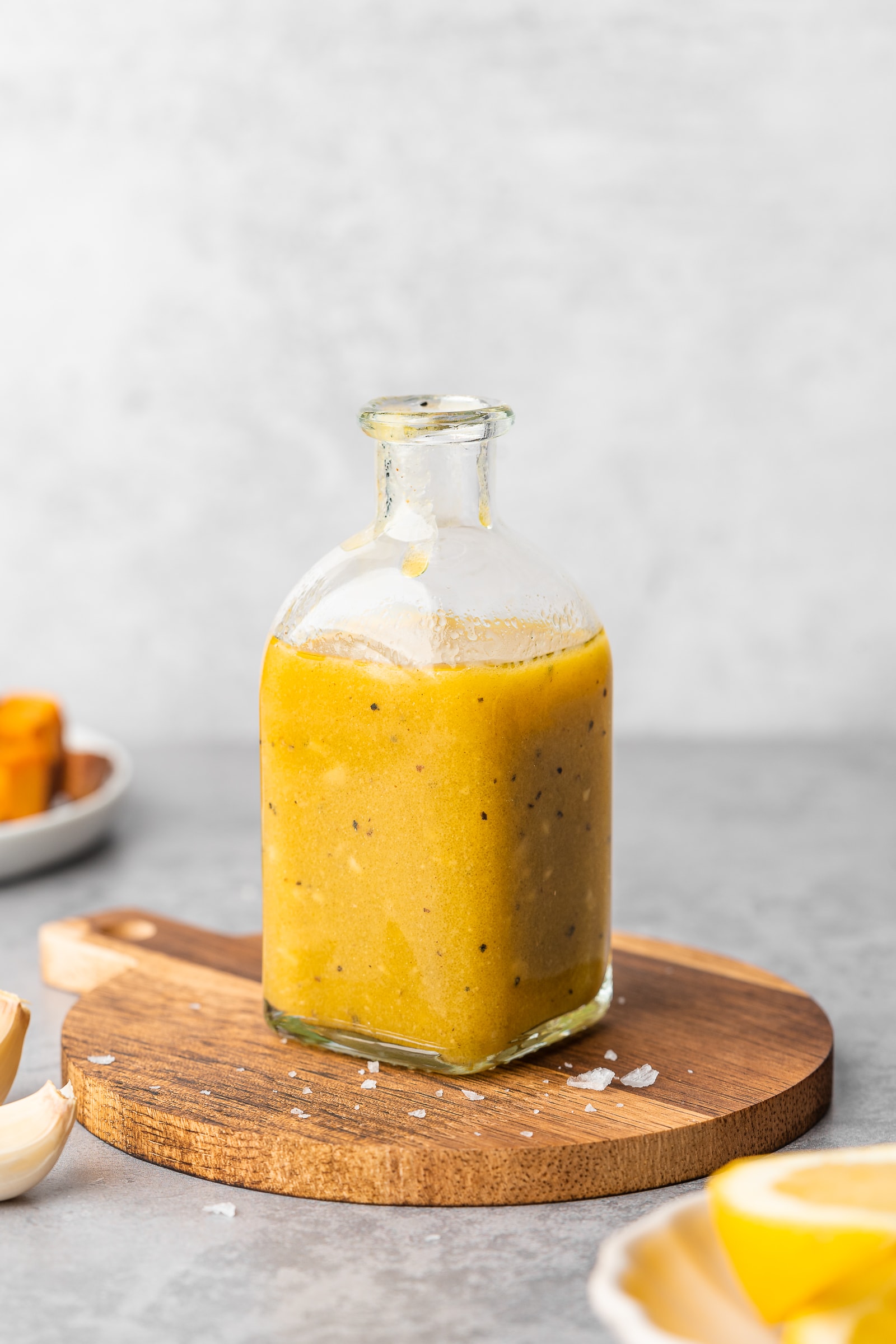 Maple dijon vinaigrette in small glass jar on wood cutting board.