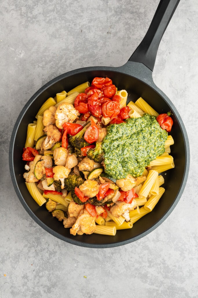 Cooked pasta, vegetables, and pesto in a pan.