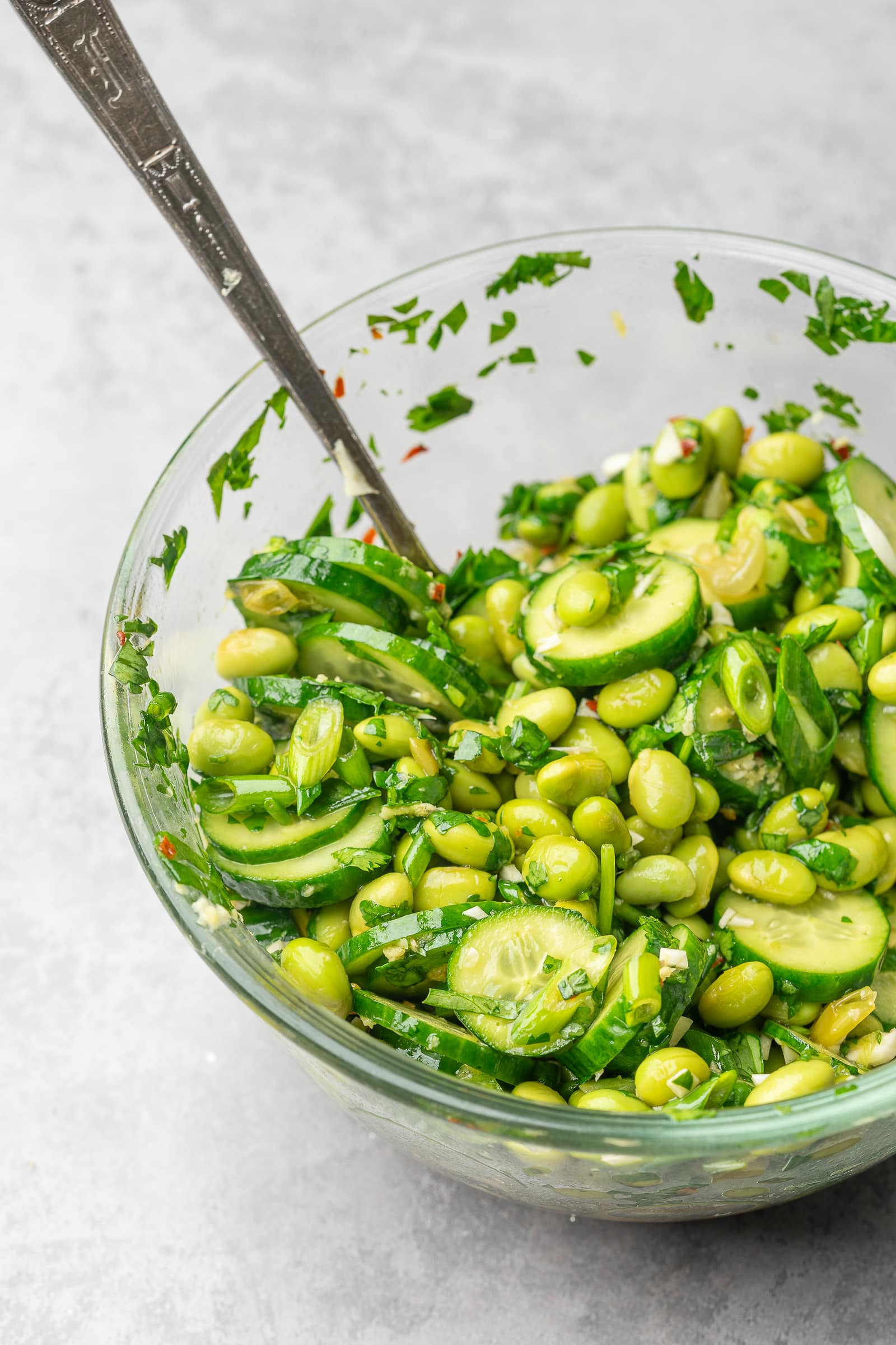 Edamame cucumber salad mixed together with dressing in a glass bowl.