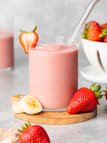 Almond milk strawberry smoothie in a glass cup garnished with strawberry slice.