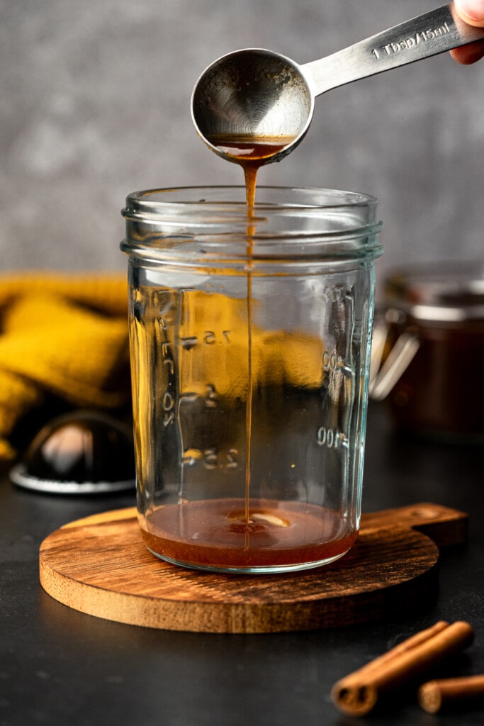 Apple brown sugar syrup being poured into a glass jar.