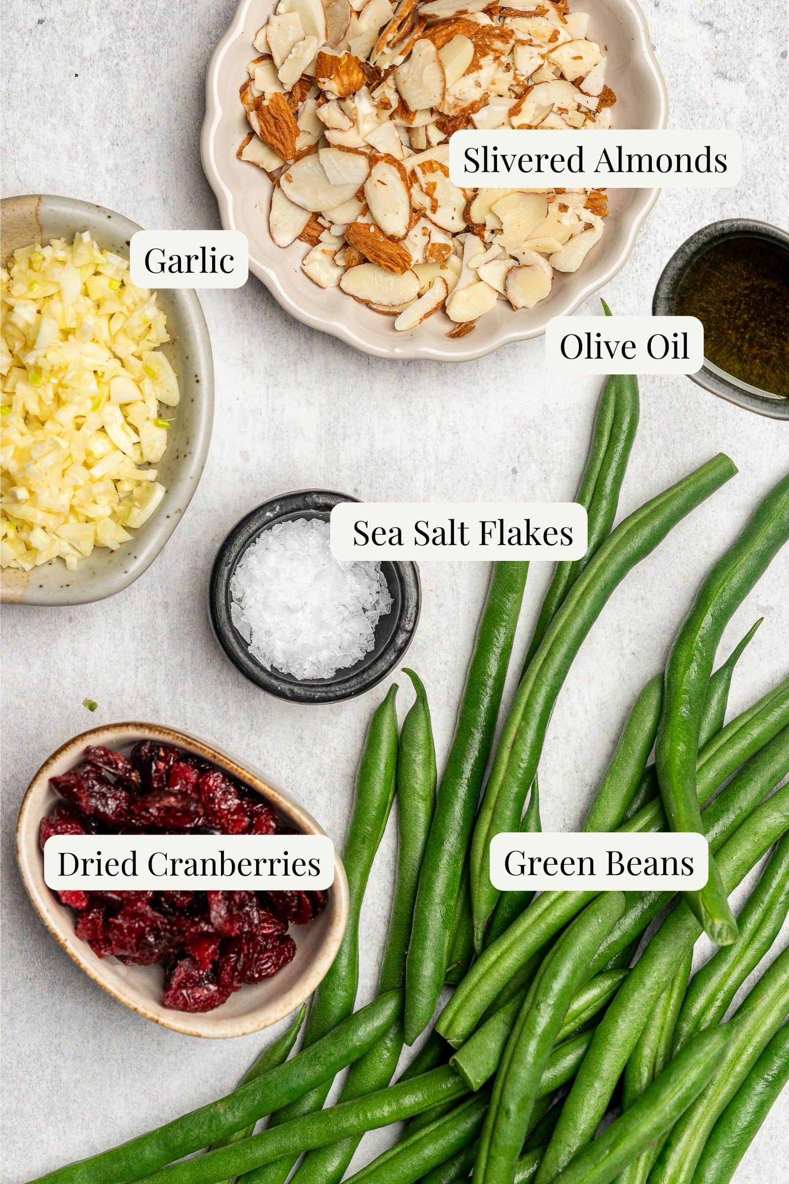 Ingredients for green beans with cranberries and almonds separated into small bowls and labeled.