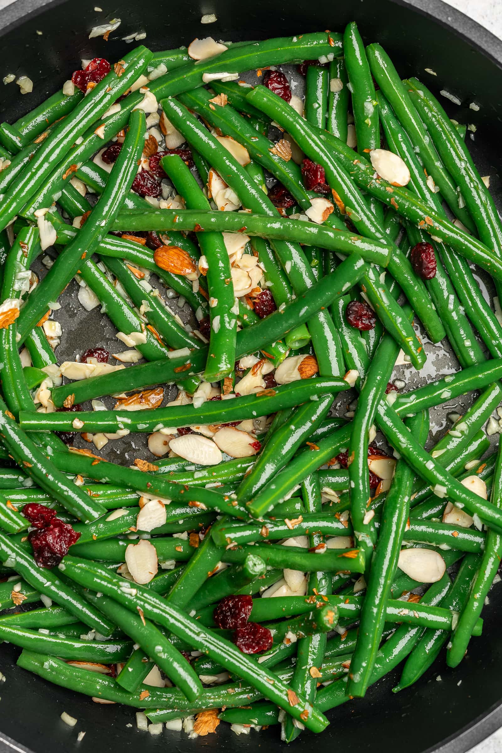 Garlic green beans with cranberries and almonds in a frying pan.