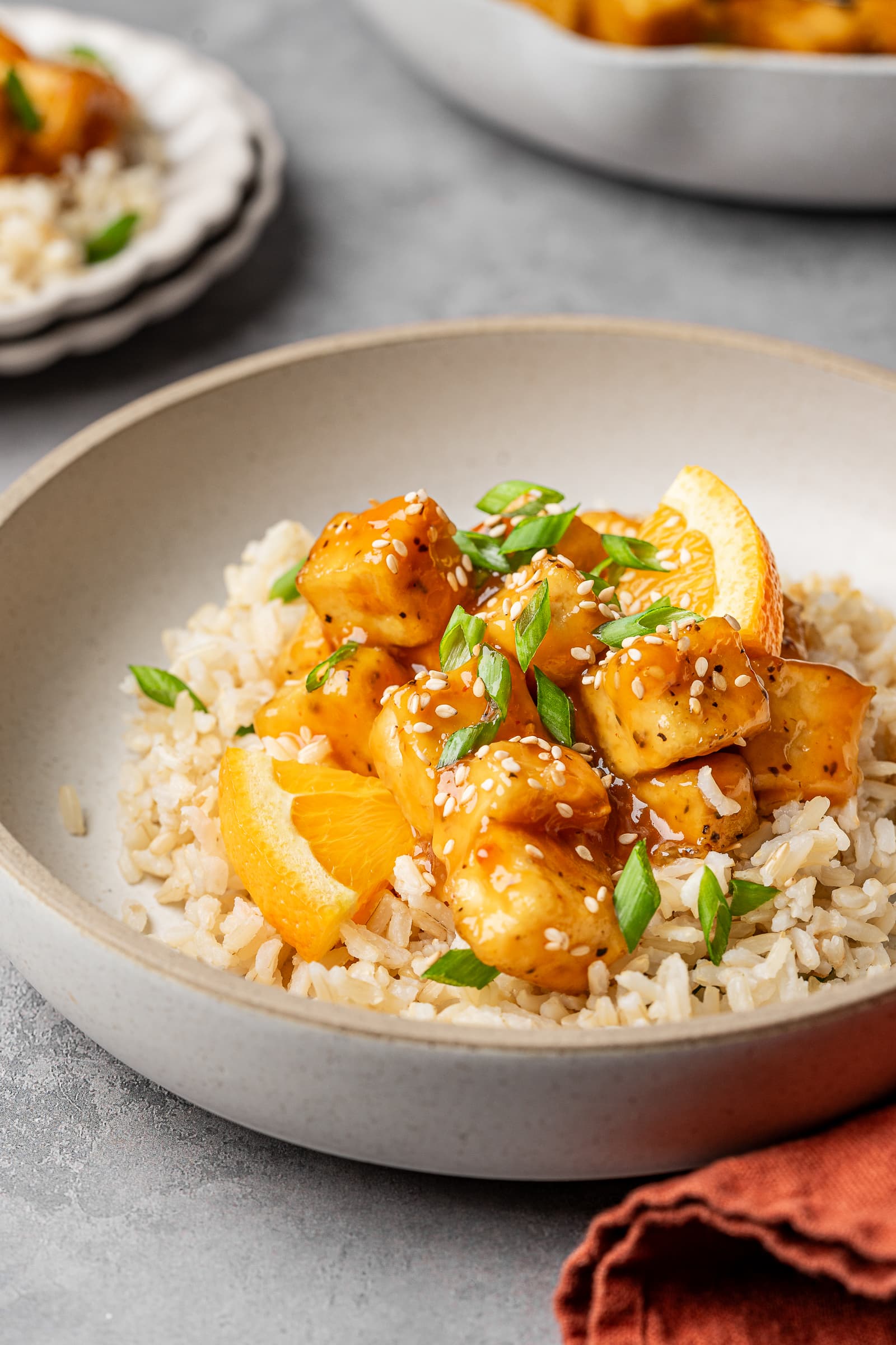 Orange tofu served over brown rice and garnished with sesame seeds and green onions.
