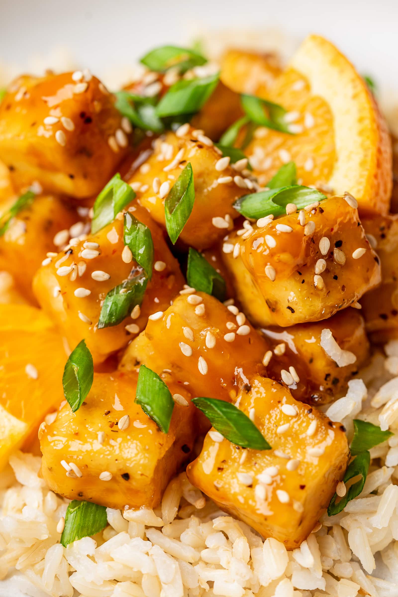 Close up of orange tofu garnished with sesame seeds and green onion.
