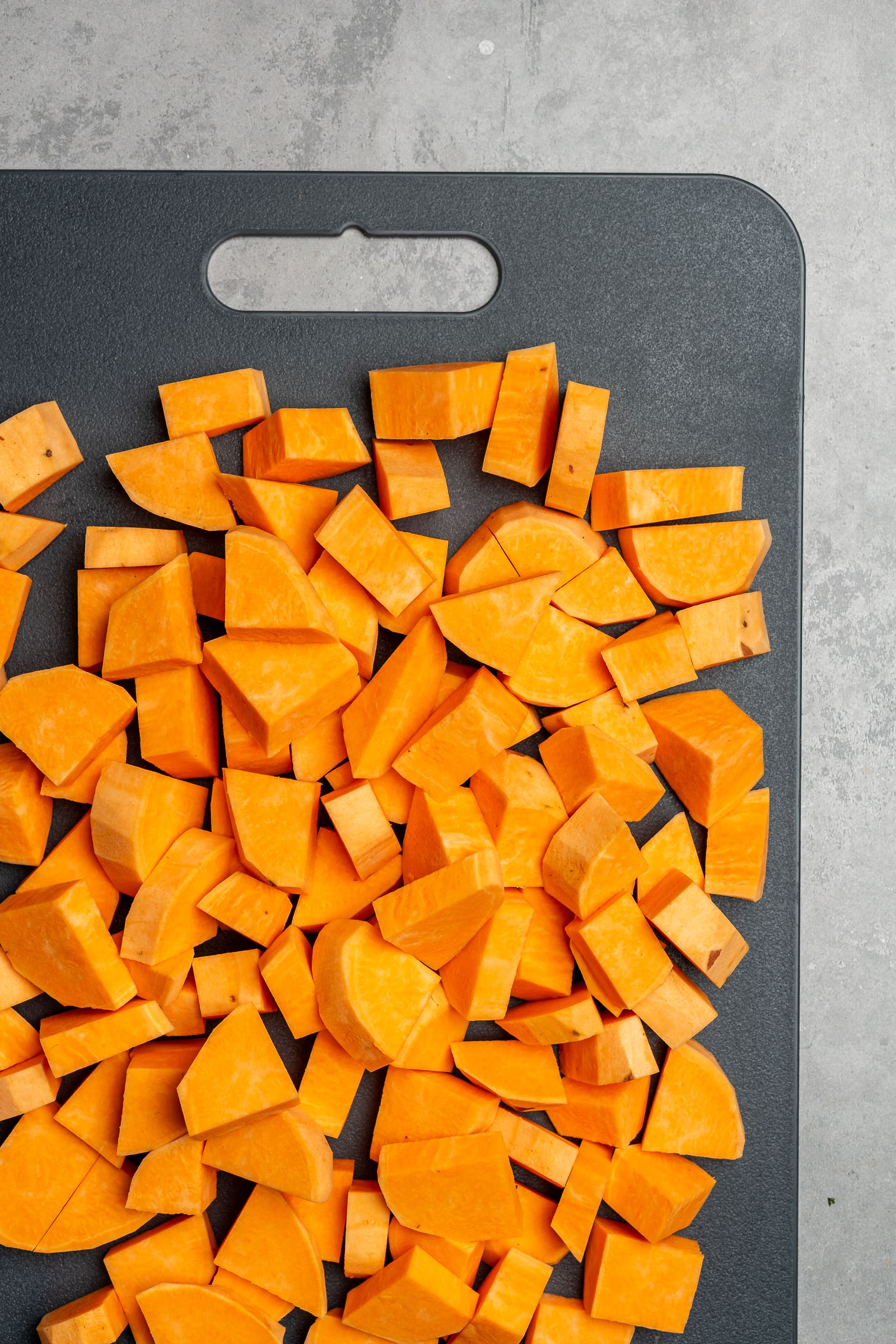 Sweet potatoes diced on a gray cutting board.