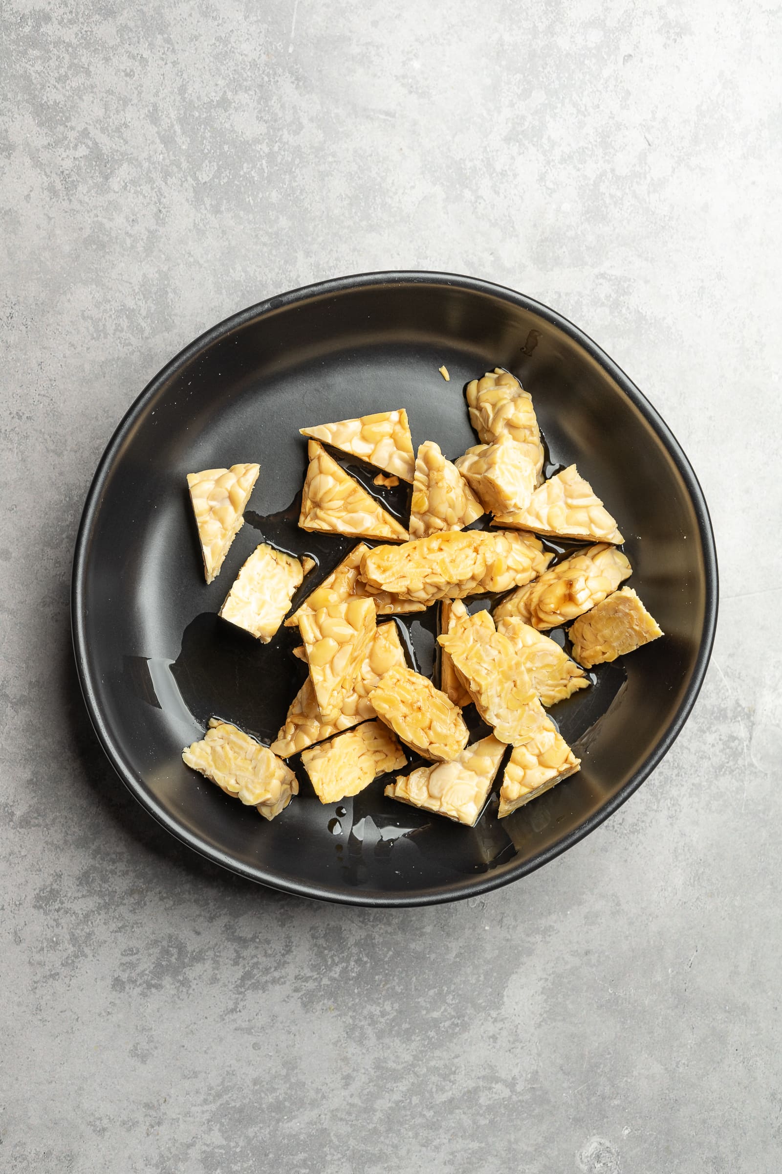 Tempeh cut in small triangles and placed in a large shallow bowl with soy sauce.