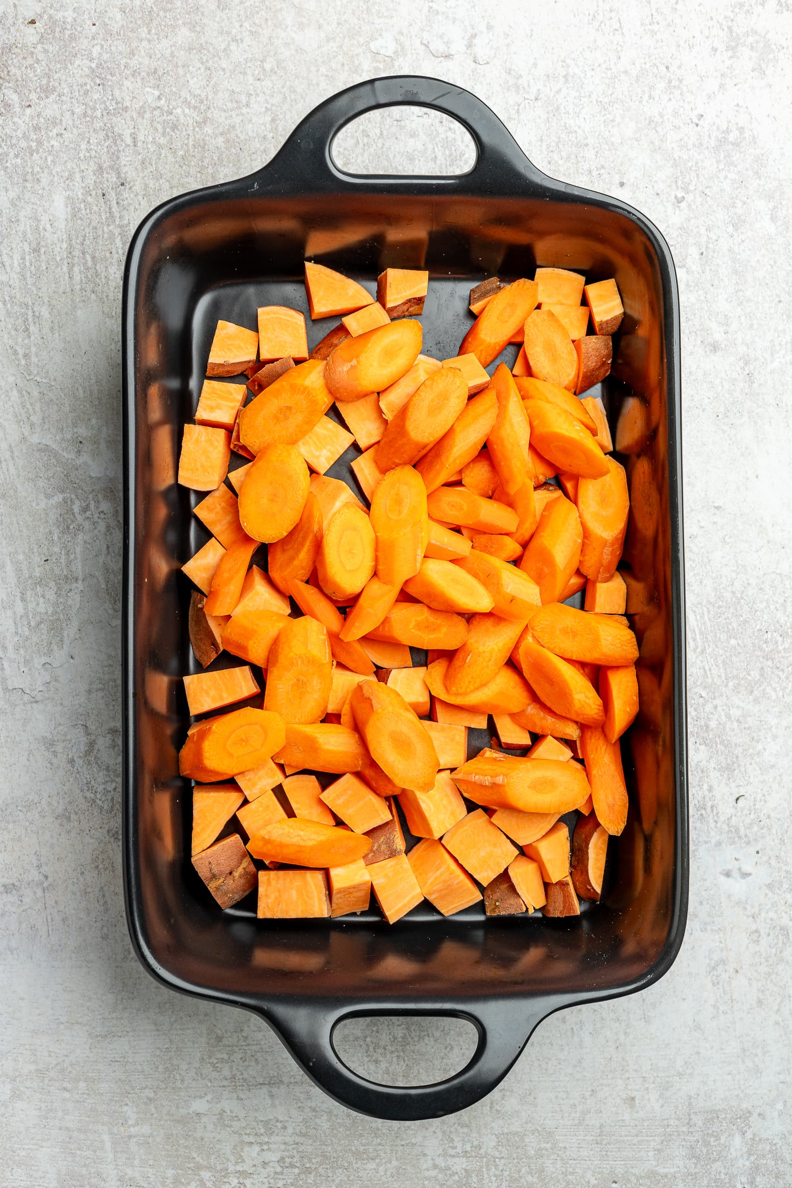 Chopped sweet potatoes and carrots in a large baking dish.