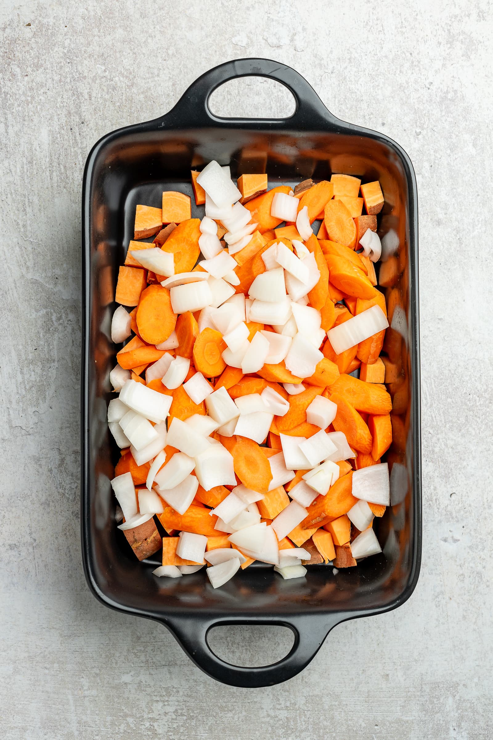 Chopped potatoes, carrots, and onions in a large baking dish.