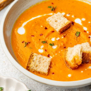 Roasted sweet potato soup in a serving bowl garnished with thyme, red pepper flakes, and croutons.