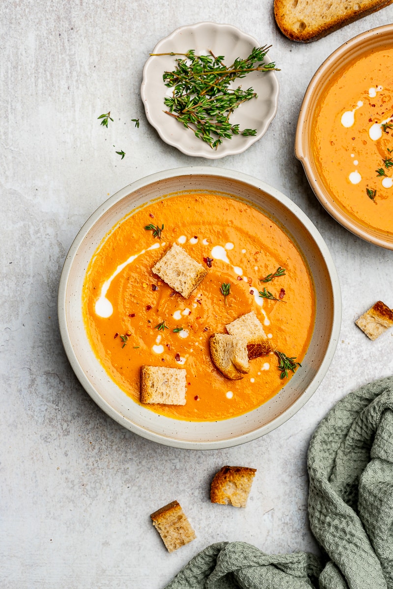 Roasted sweet potato soup in a serving bowl garnished with thyme, red pepper flakes, and croutons.