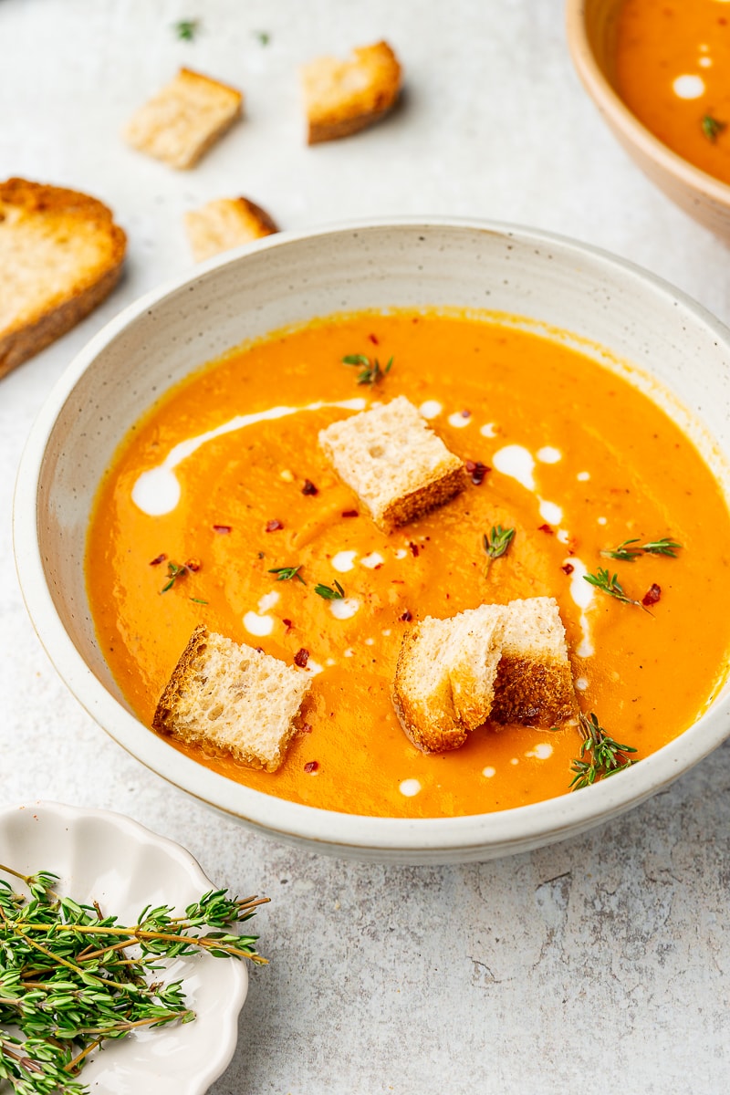 Roasted sweet potato soup in a serving bowl garnished with thyme, red pepper flakes, and croutons.