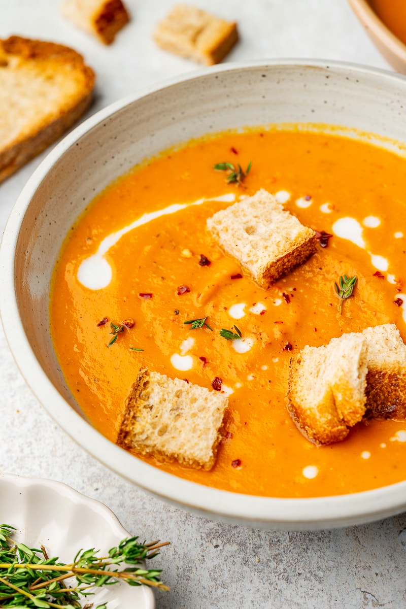 Roasted sweet potato soup in a serving bowl garnished with thyme, red pepper flakes, and croutons.
