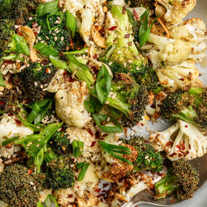 Close up of crispy broccoli and cauliflower with sesame seeds, chili flakes, and green onions.