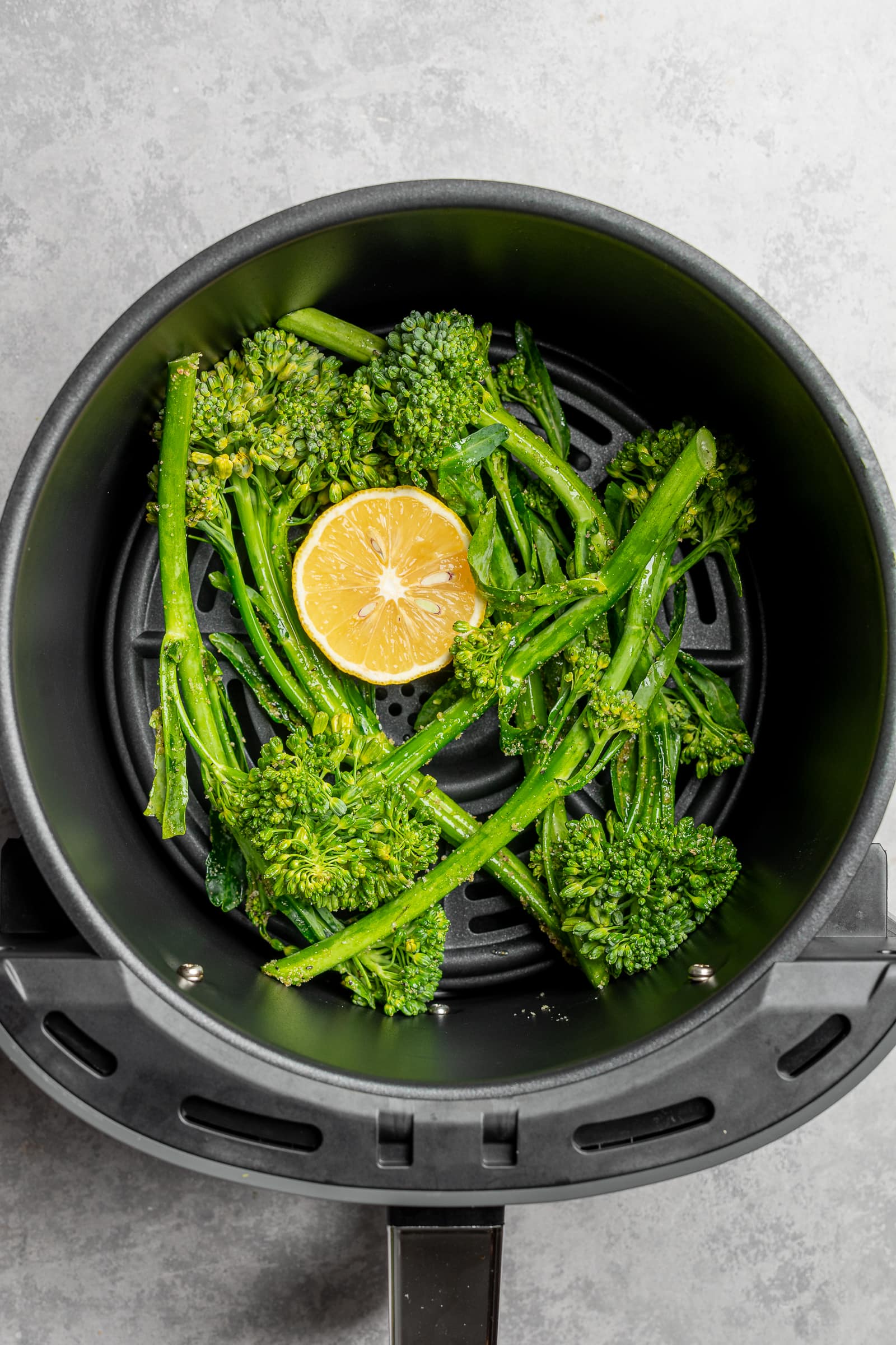 Broccolini in an air fryer basket with a lemon.