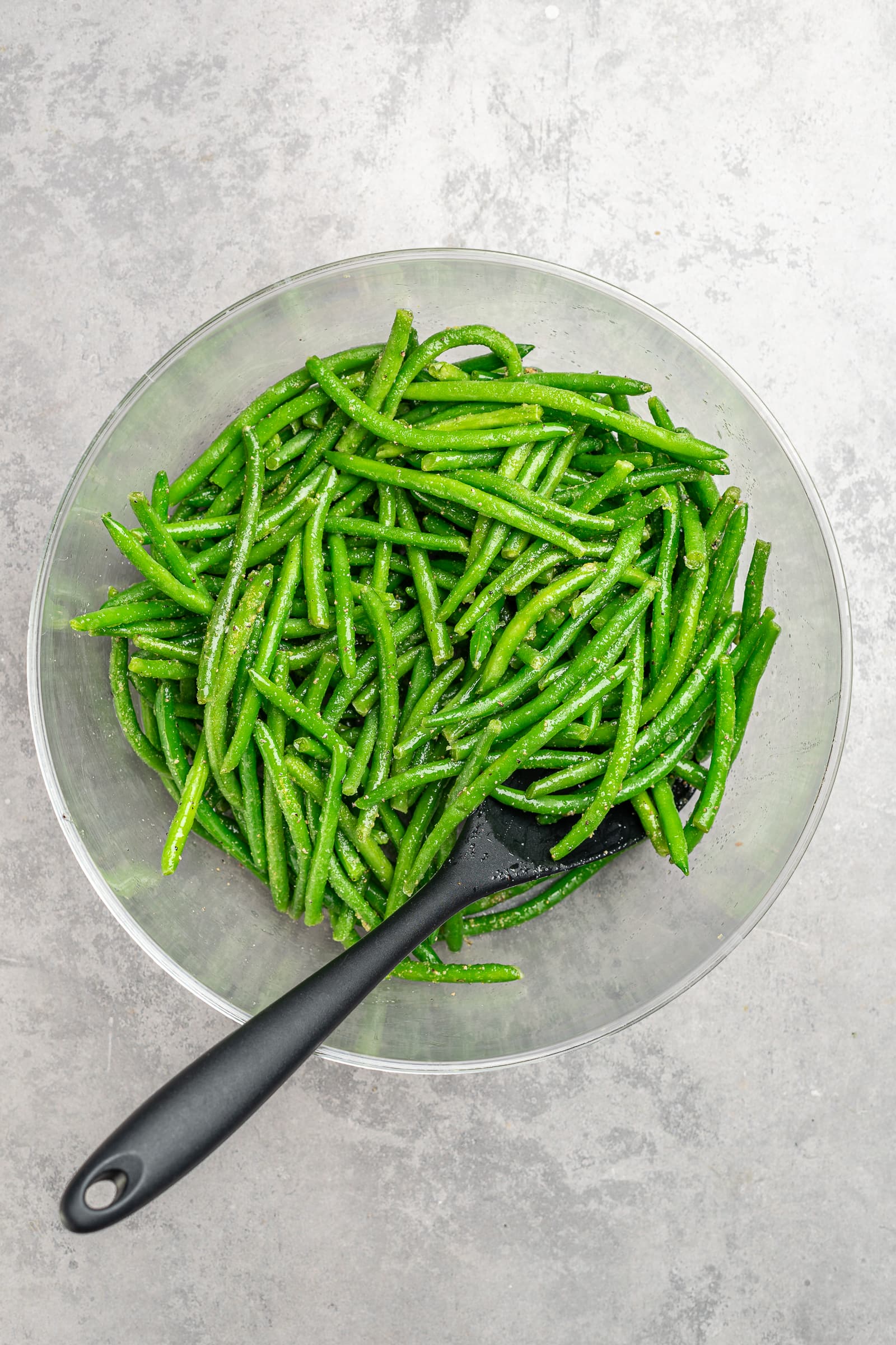 Frozen green beans in a large bowl tossed in seasonings.