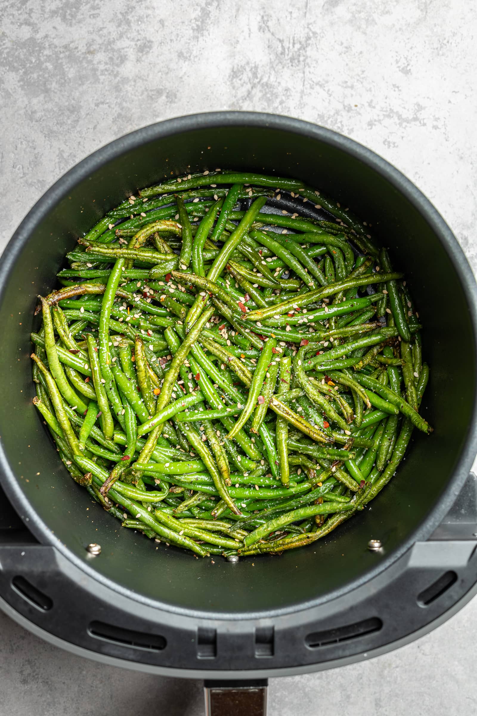 Air fried green beans in an air fryer with sesame seeds and red chili flakes.