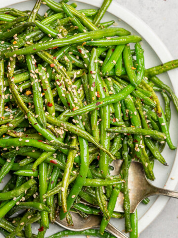 Air fried green beans on a serving plate with sesame seeds and red chili flakes.