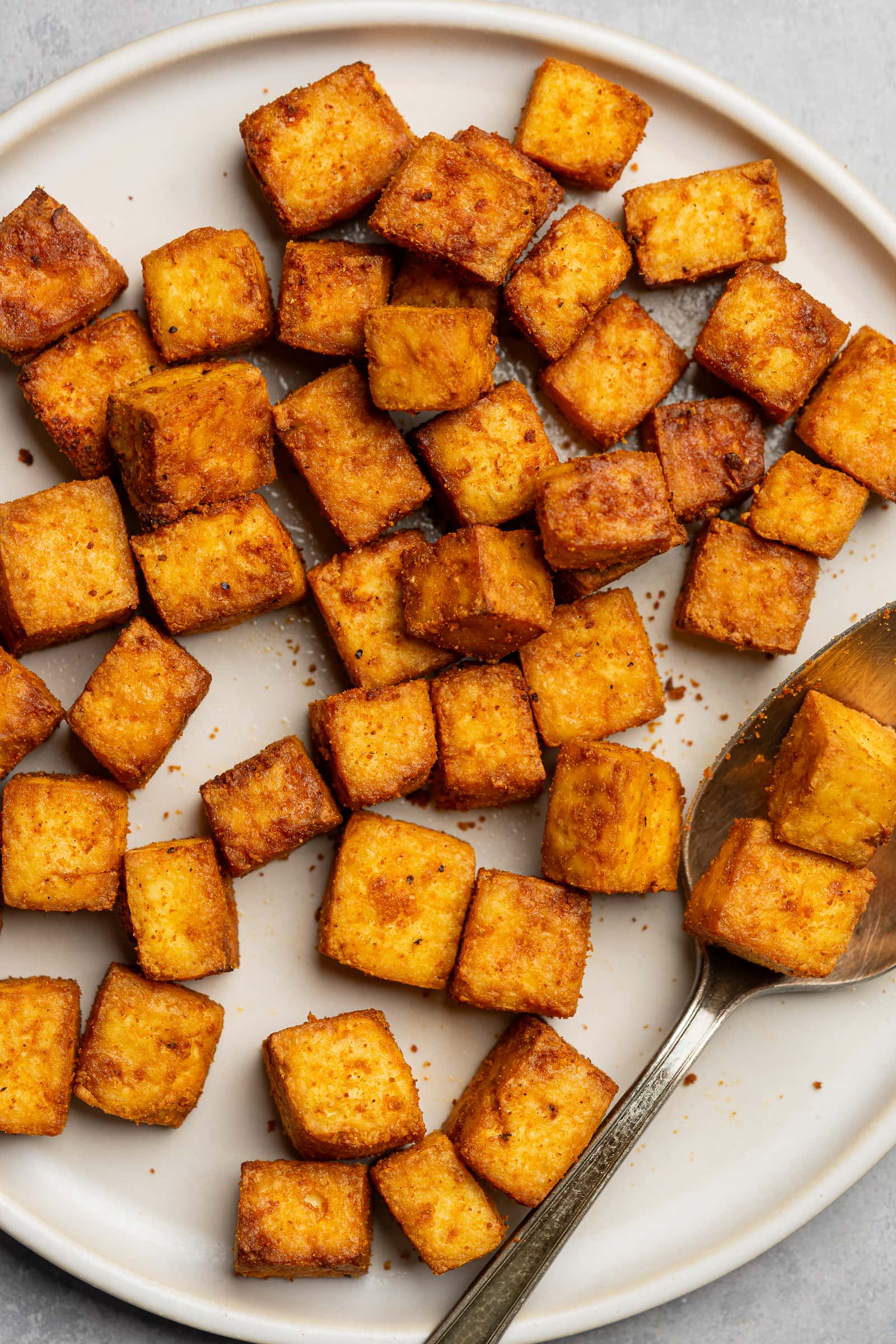 Crispy air fryer tofu on a serving plate with a serving spoon.