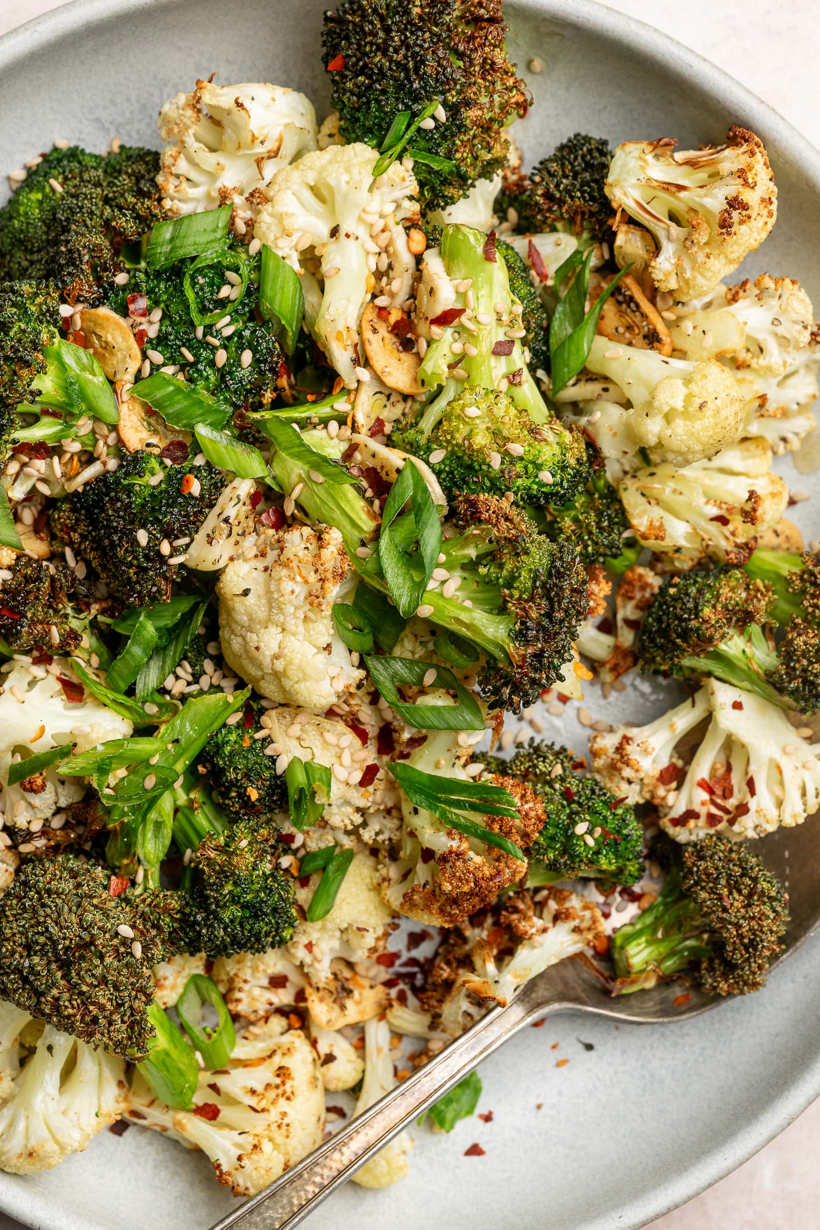 Close up of crispy broccoli and cauliflower with sesame seeds, chili flakes, and green onions.