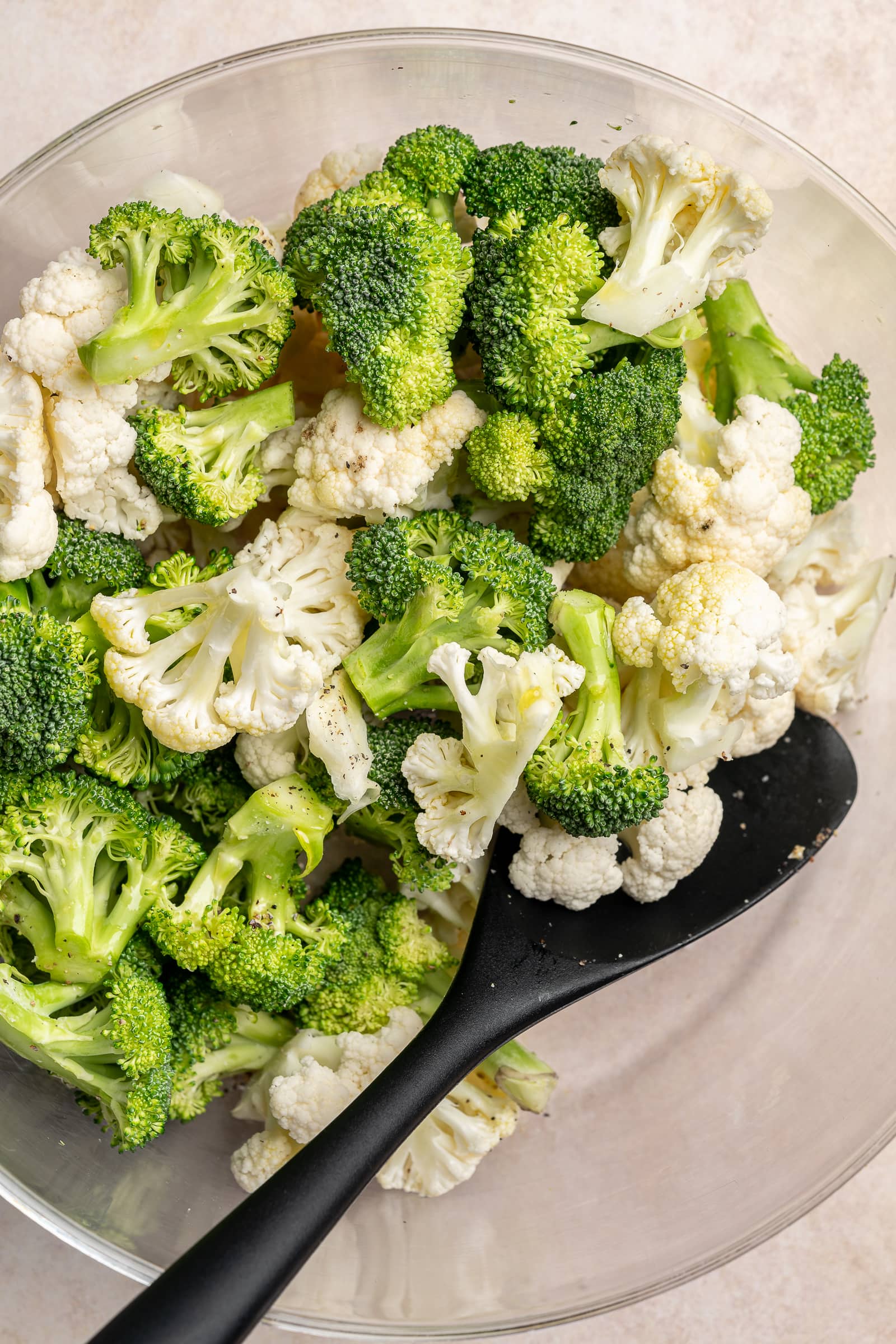 garlic, broccoli, and cauliflower in a large bowl being tossed with olive oil, salt, and pepper.