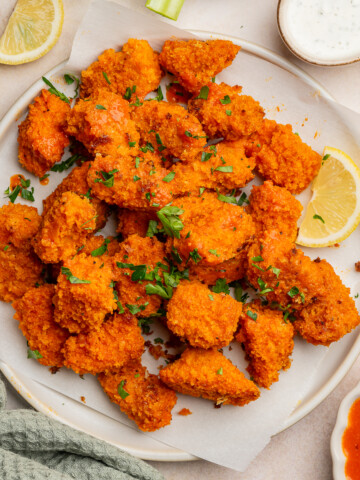 Buffalo tempeh nuggets on a serving plate with a side of ranch and garnished with parsley.