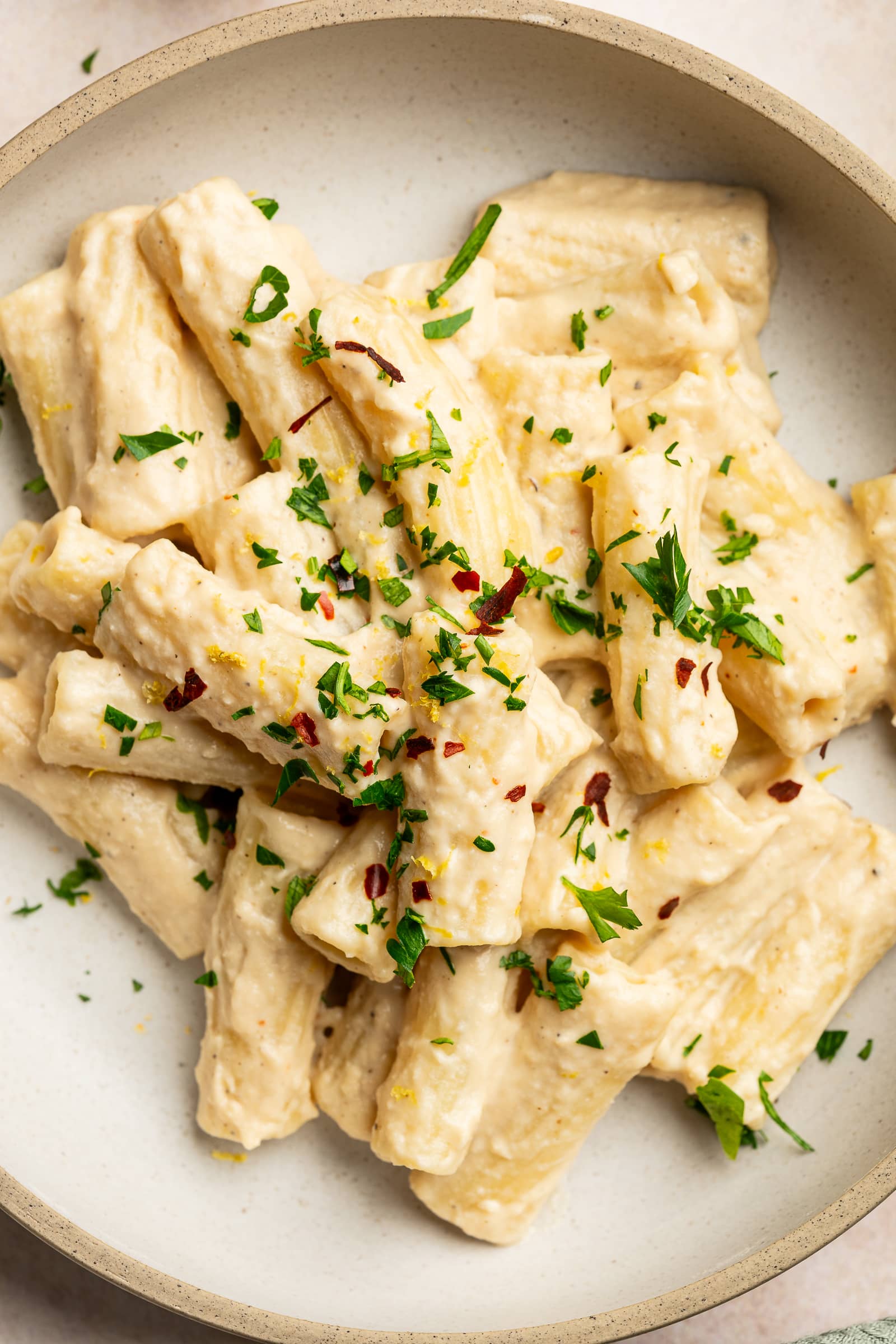 Cashew pasta garnished with red chili flakes, parsley, and lemon zest in a serving bowl.