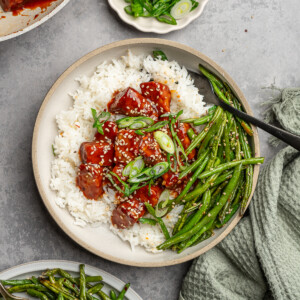 Gochujang tempeh served over jasmine rice with a side of green beans and garnished with sesame seeds and green onions.