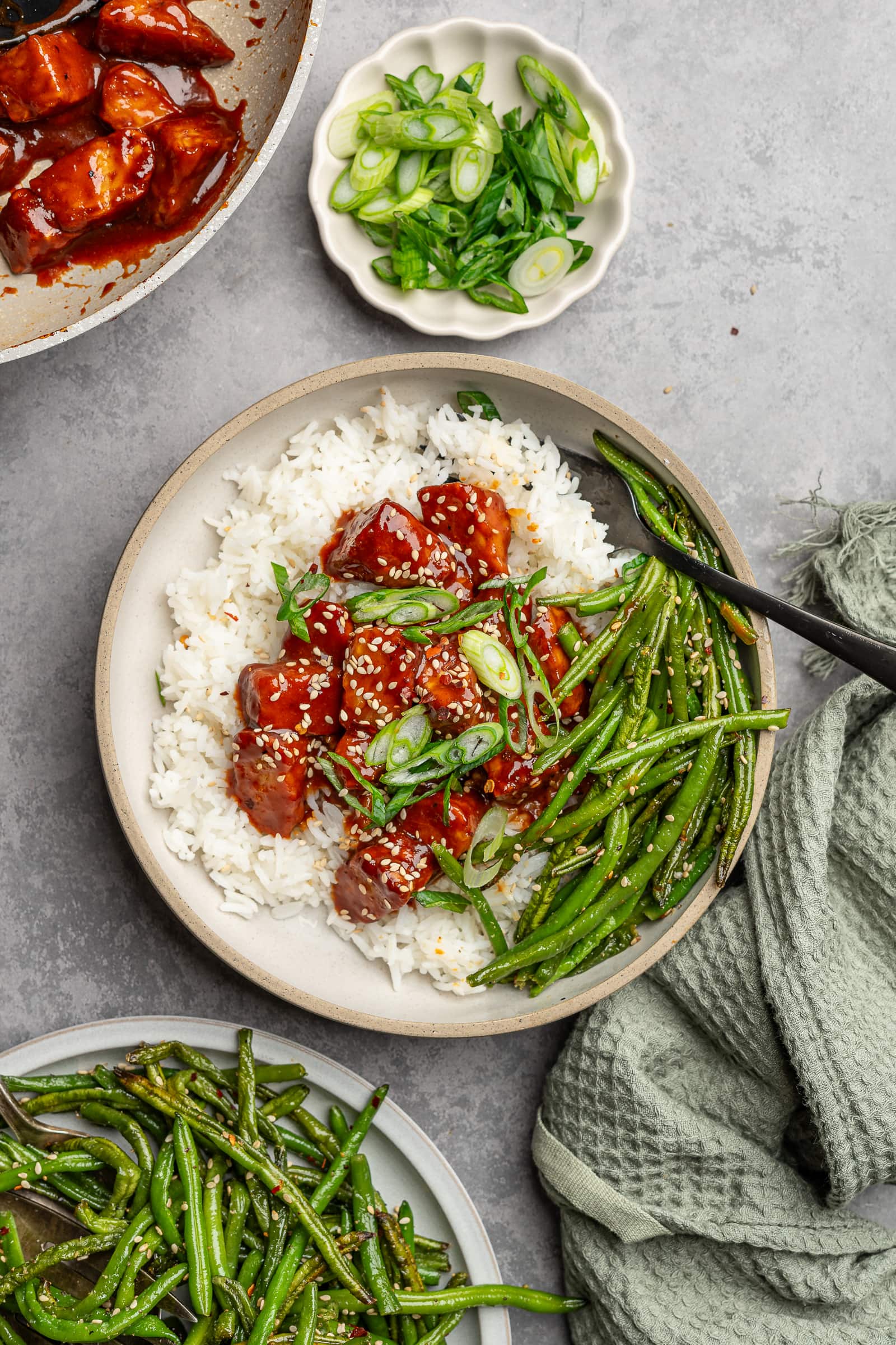 Gochujang tempeh served over jasmine rice with a side of green beans and garnished with sesame seeds and green onions.