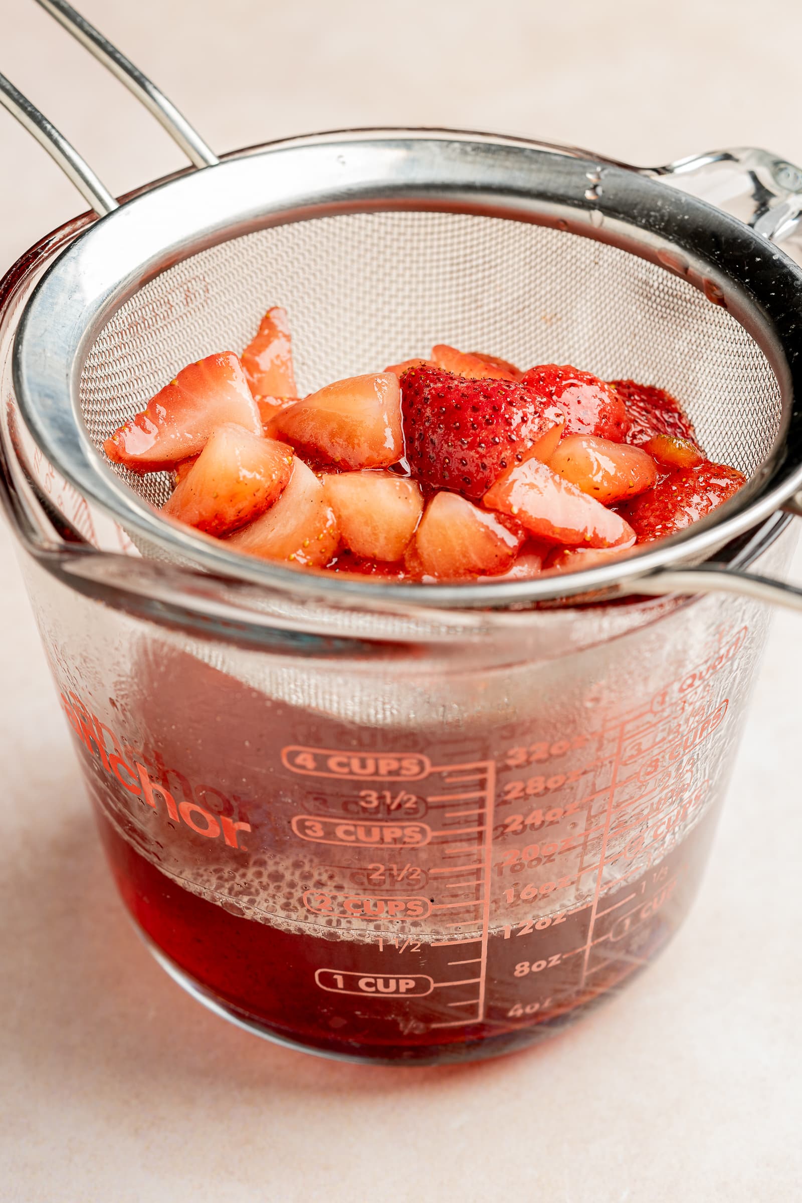 Simmered strawberry simple syrup being strained through a fine mesh strainer.