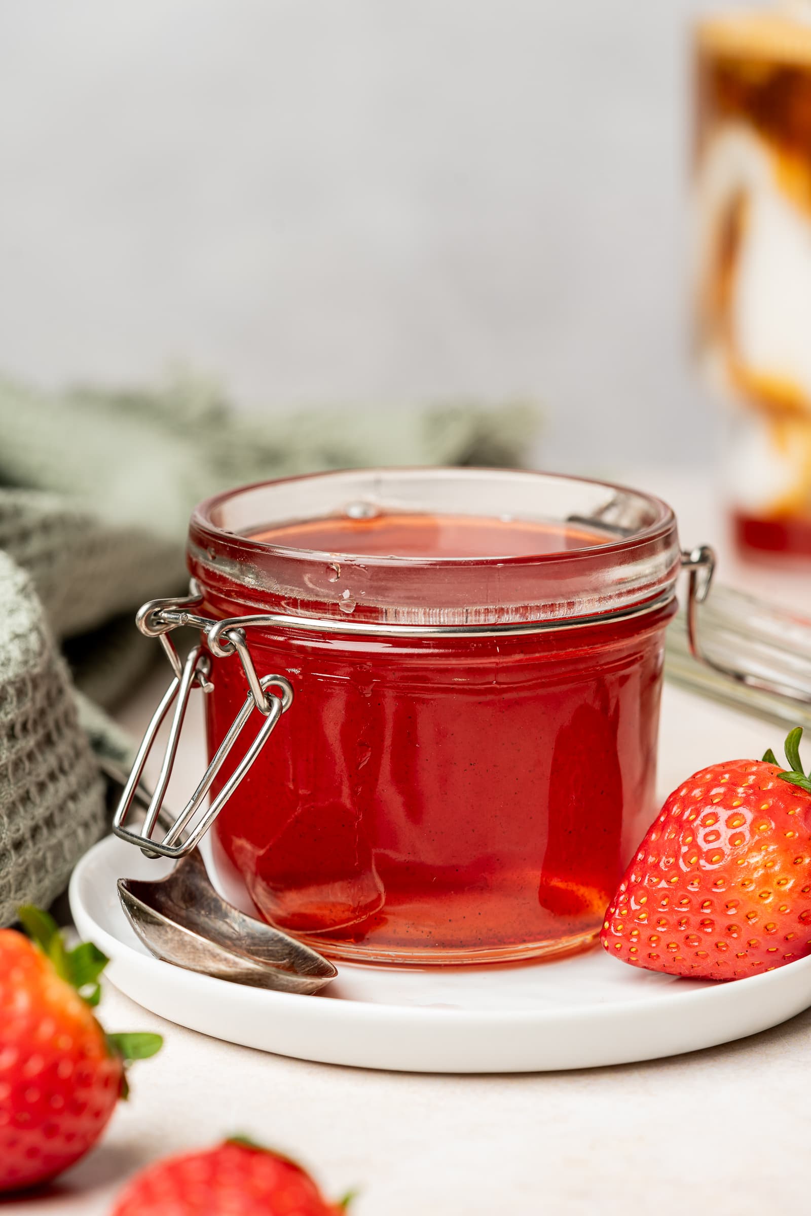Strawberry simple syrup in a small jar on a white plate and surrounded by strawberries.