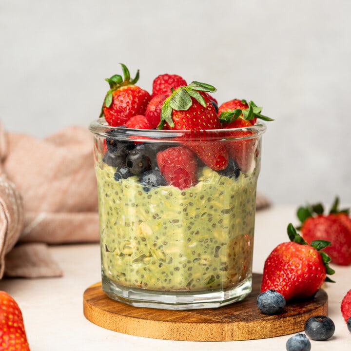 A glass jar of matcha oats with strawberries, blueberries, and raspberries.