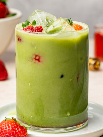 Iced matcha with strawberry syrup in a glass with fresh strawberries as a garnish.