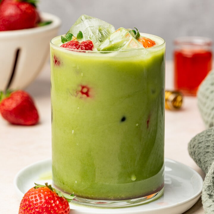 Iced matcha with strawberry syrup in a glass with fresh strawberries as a garnish.