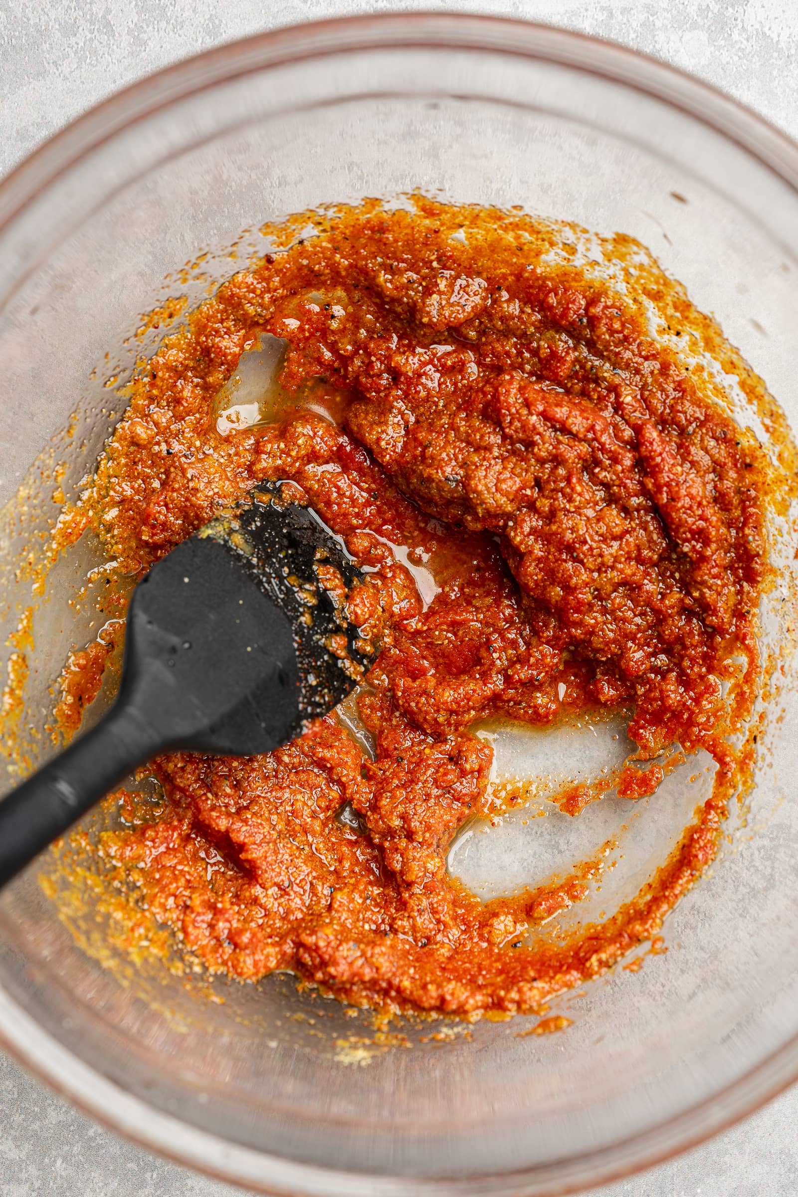 Tomato paste, soy sauce, olive oil, and seasonings mixed together in a large glass bowl.