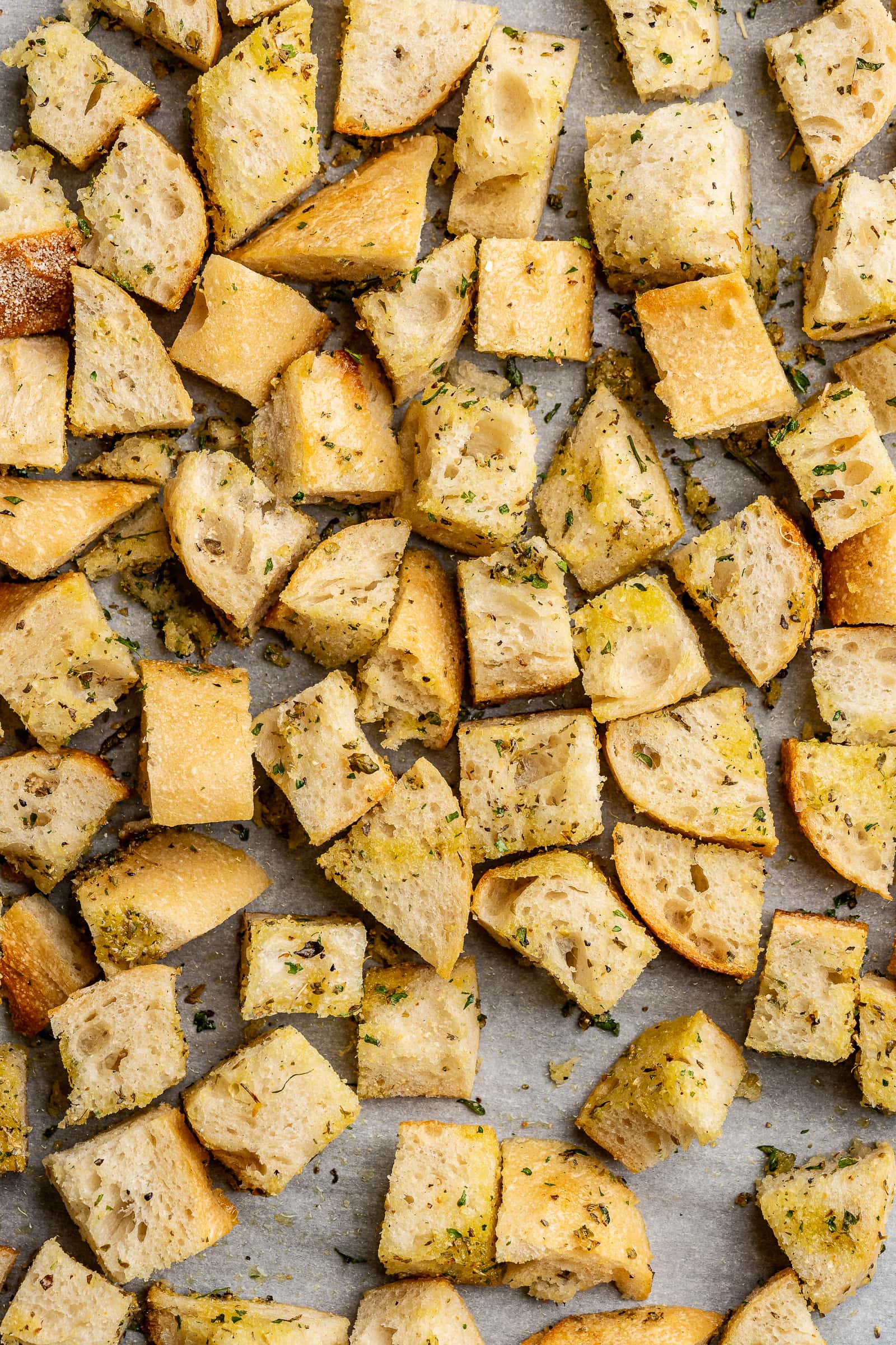 Cubed bread tossed with olive oil, dried herbs, and seasonings on parchment paper.