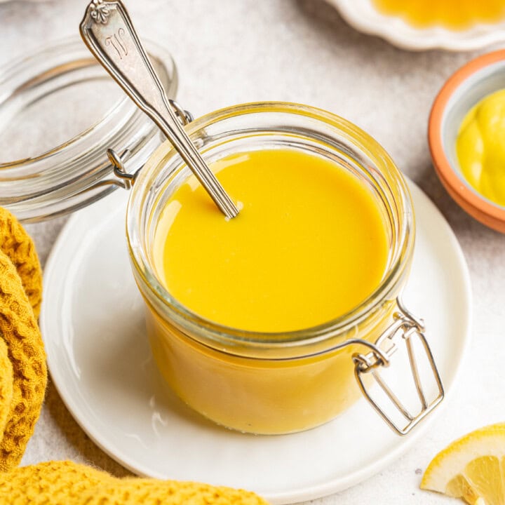 Honey mustard in a small jar sitting on a plate with a serving spoon.