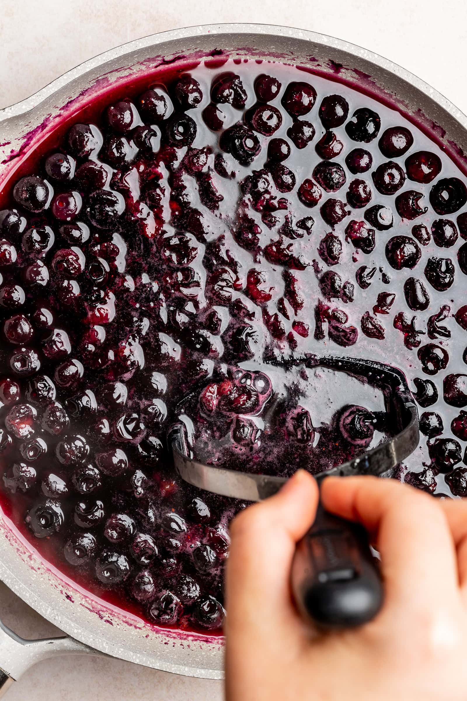Blueberry syrup being mashed with a potato masher.