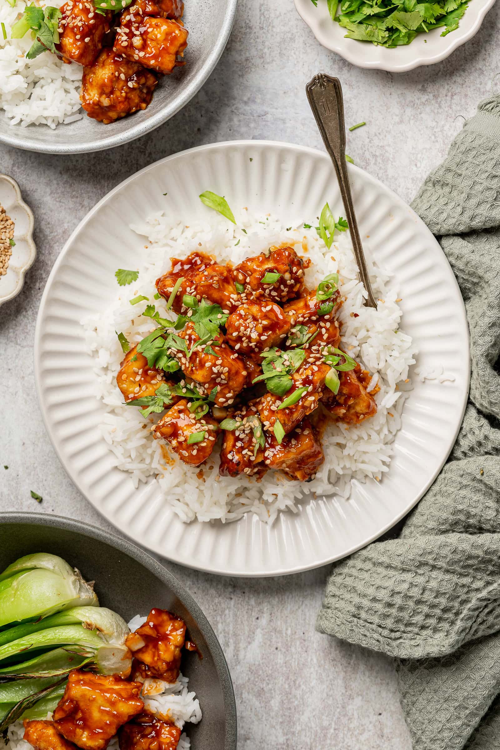 Sticky tofu on a serving of white rice and garnished with green onions and cilantro.