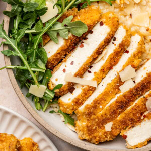 Close up of sliced tofu cutlets over a bed of arugula and creamy orzo.