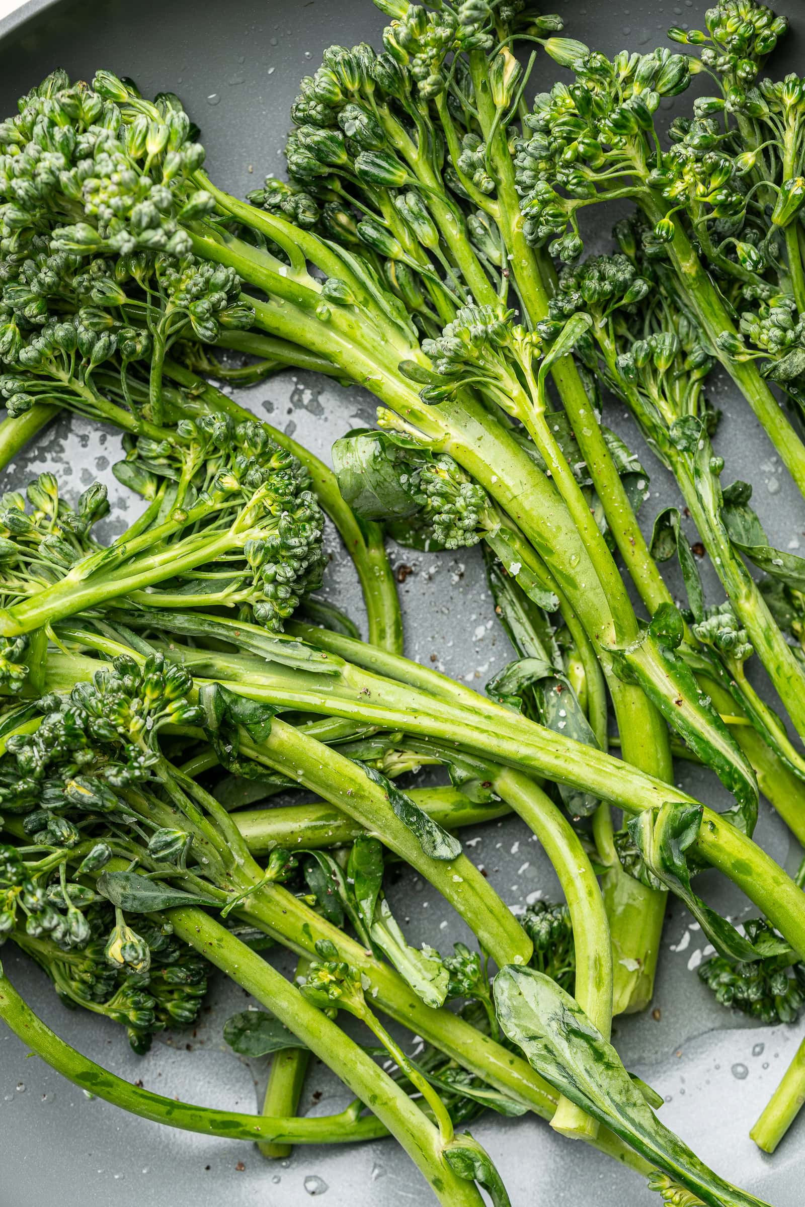 Seasoned broccolini in a frying pan.