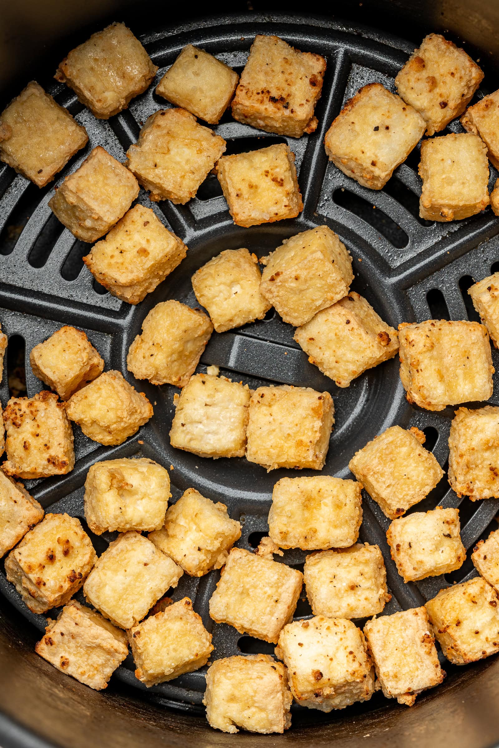 Cooked tofu in an air fryer basket.