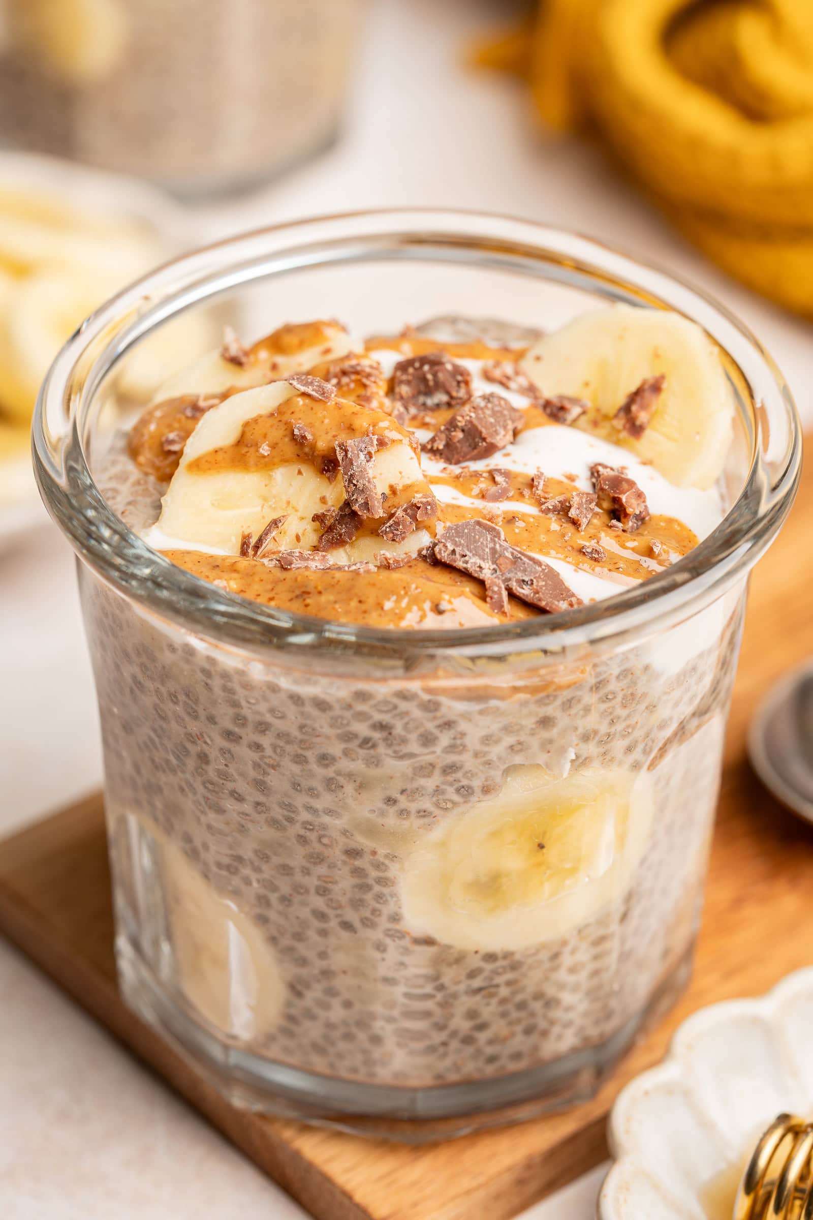 Banana chia pudding in small glass serving jar topped with bananas, almond butter, and chopped chocolate.