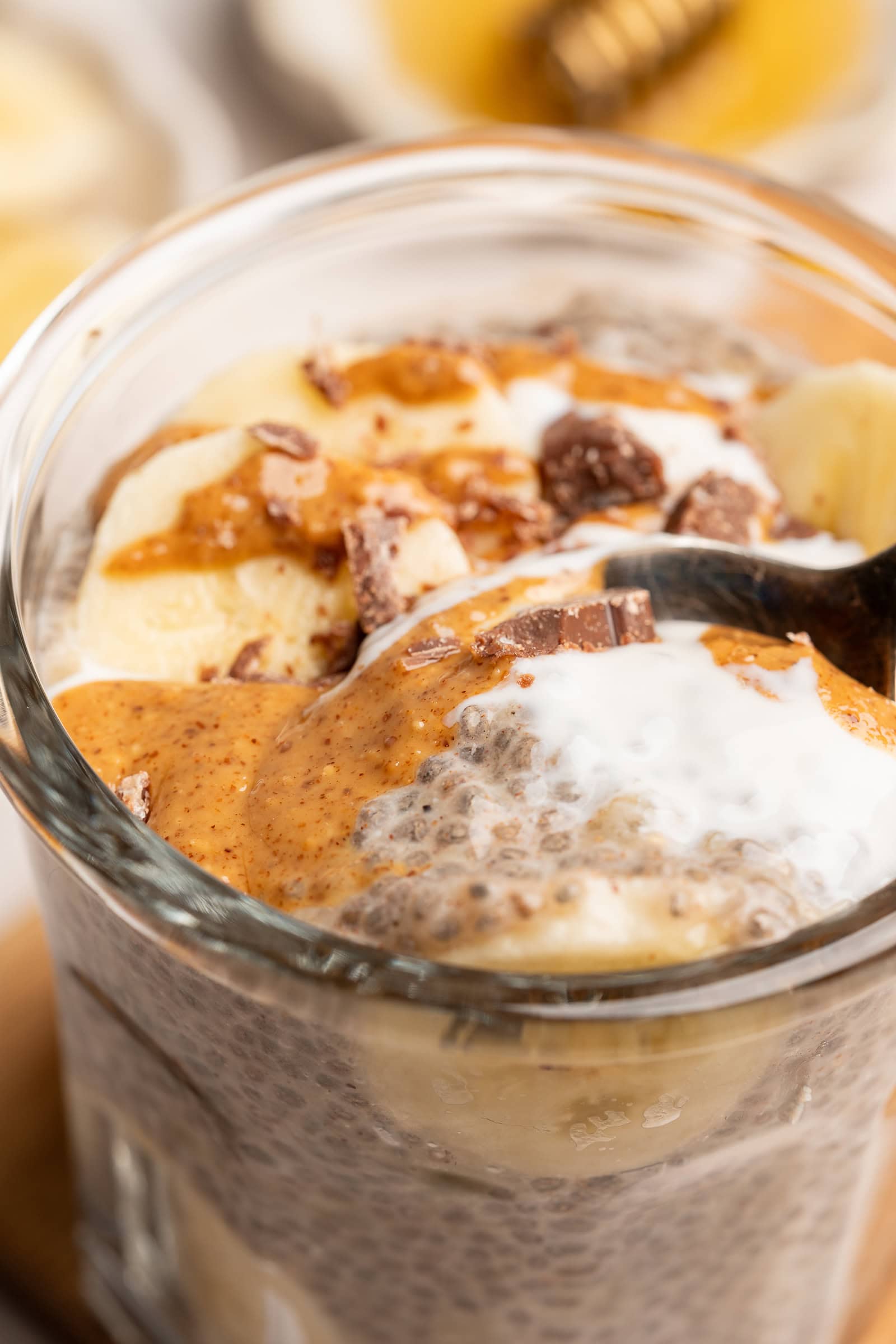 Close up of banana chia pudding in small glass serving jar topped with bananas, almond butter, and chopped chocolate.