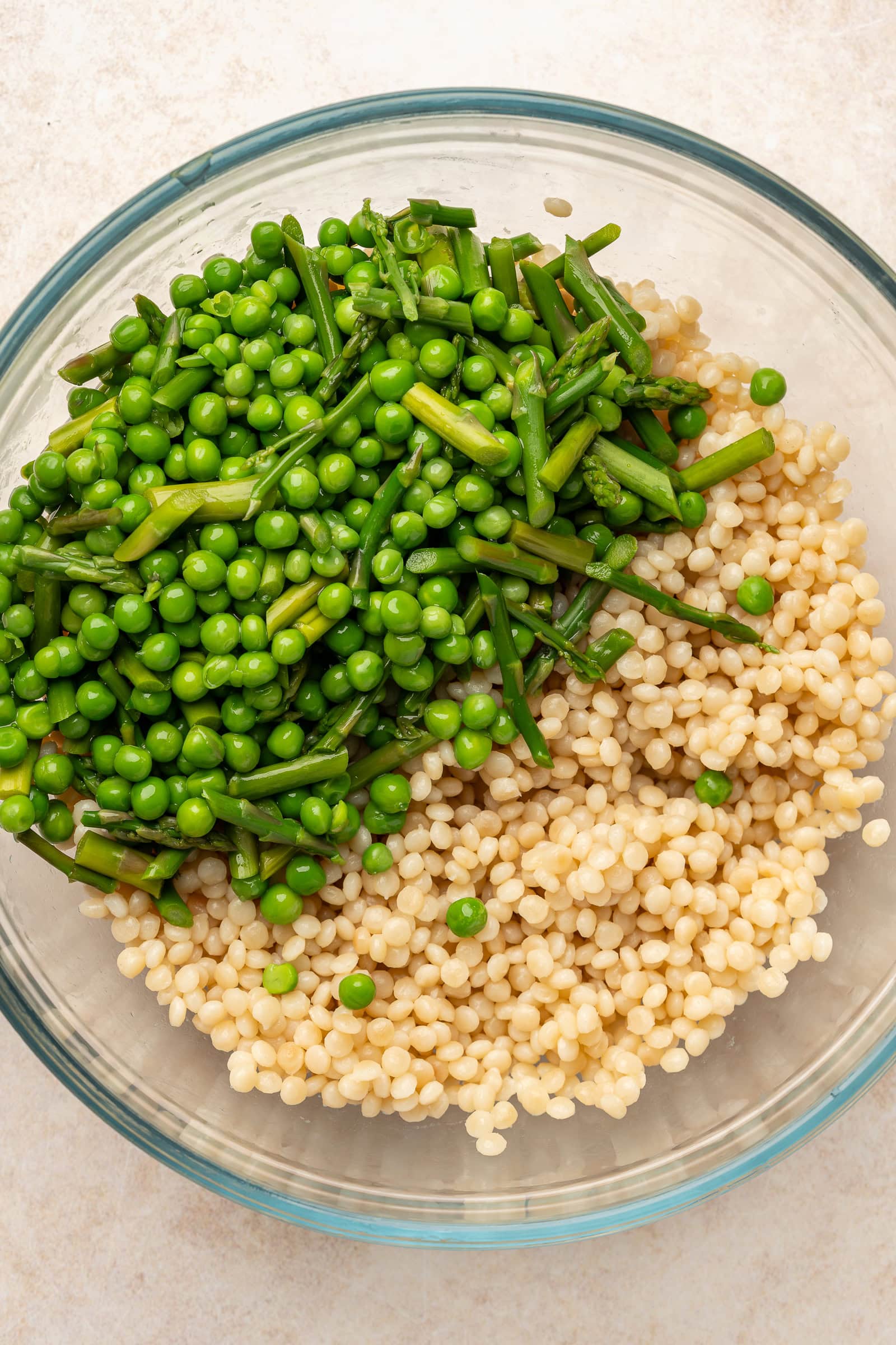 Blanched peas and asparagus on top of cooked pearl couscous in large bowl.
