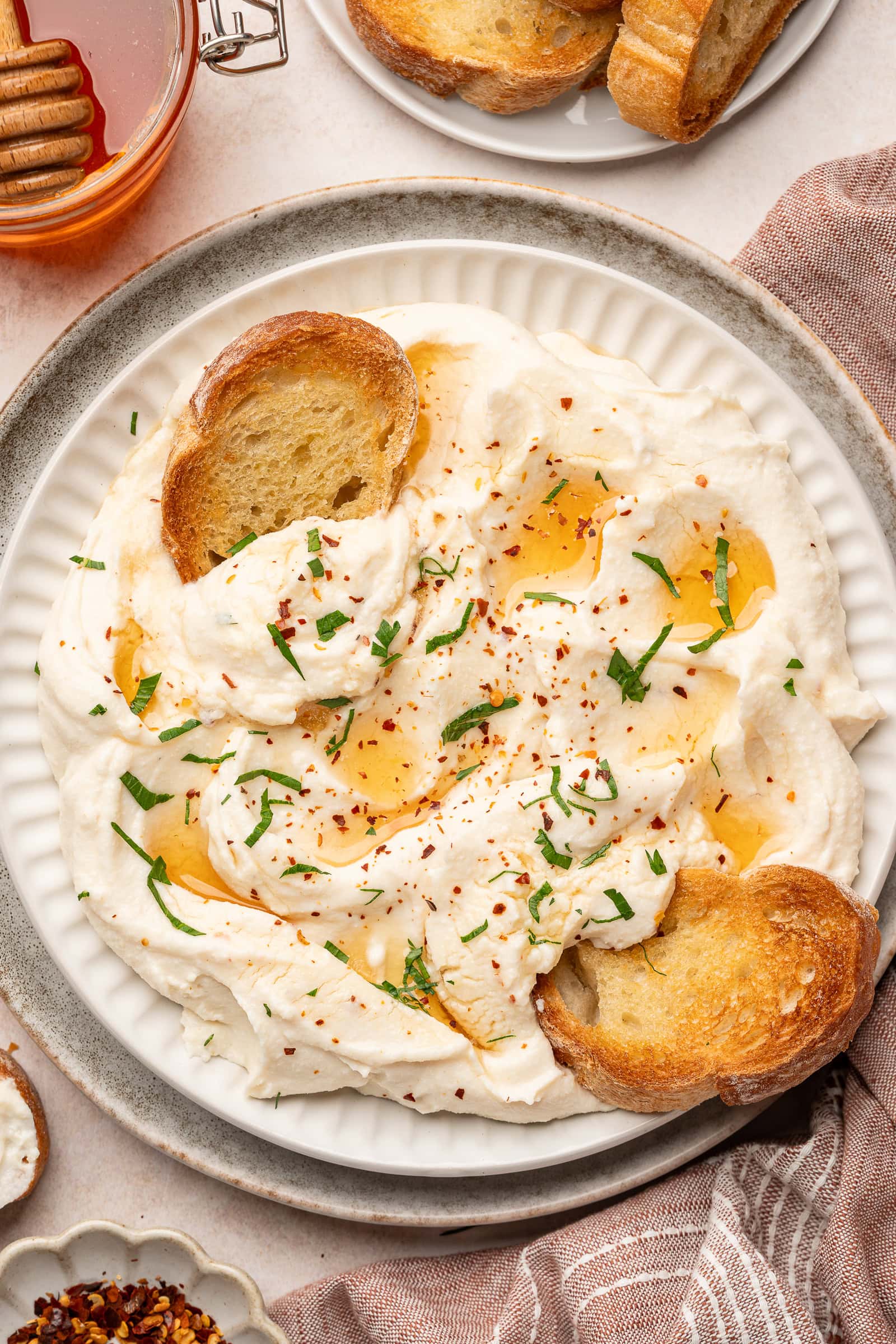 Vegan feta being plated on a serving dish, garnished with hot honey and parsley and being dipped in with toasted baguette.