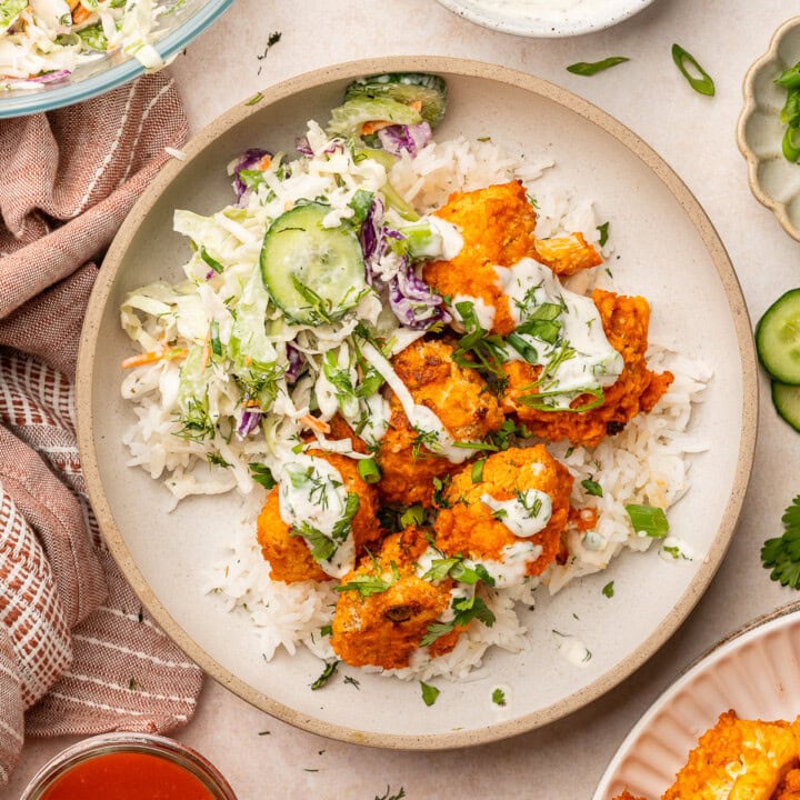 Buffalo cauliflower bites served on top of rice with cabbage cucumber slaw and vegan ranch garnished with herbs.