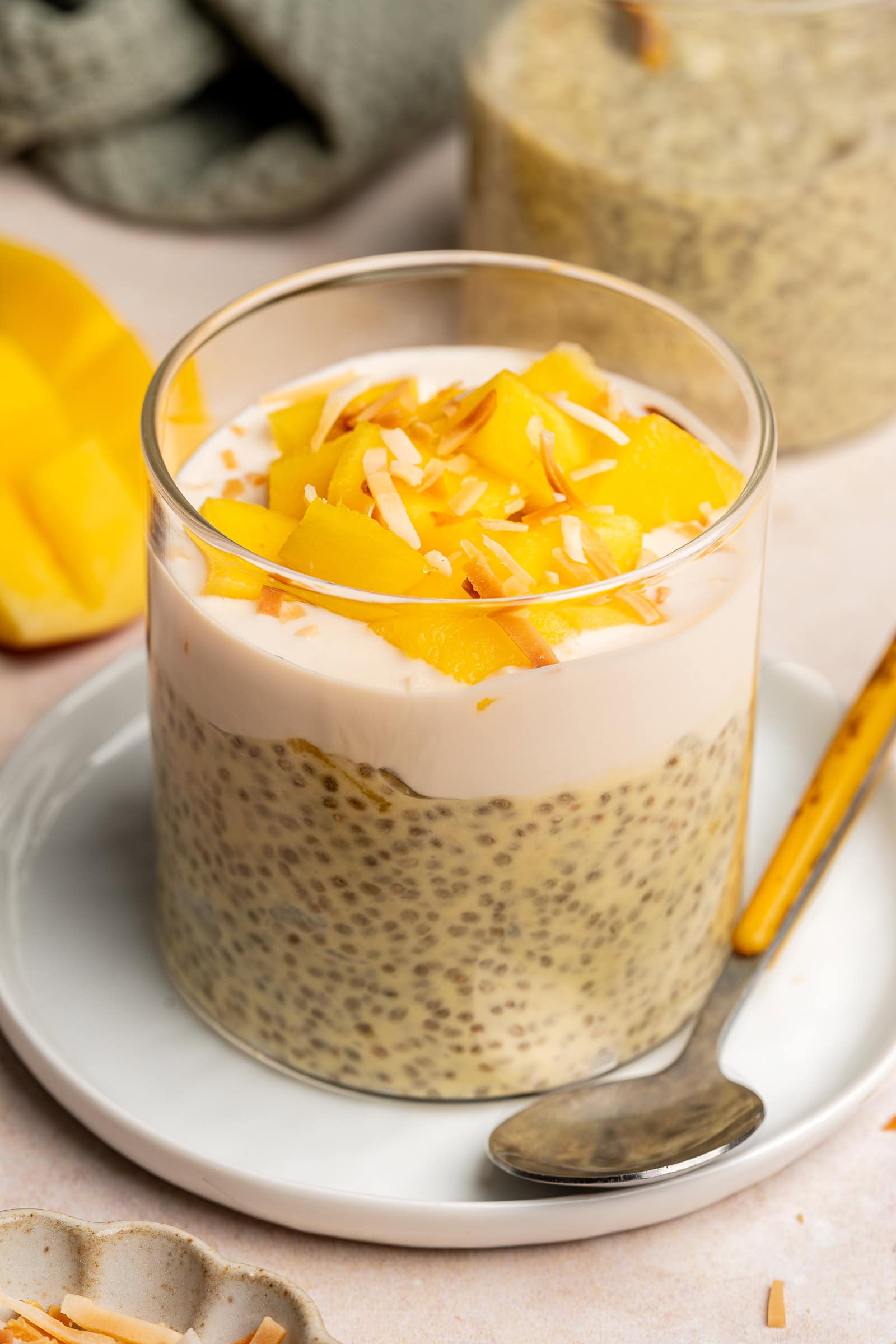 Chia pudding layered into a glass jar topped with yogurt, chunks of mango, and toasted coconut.