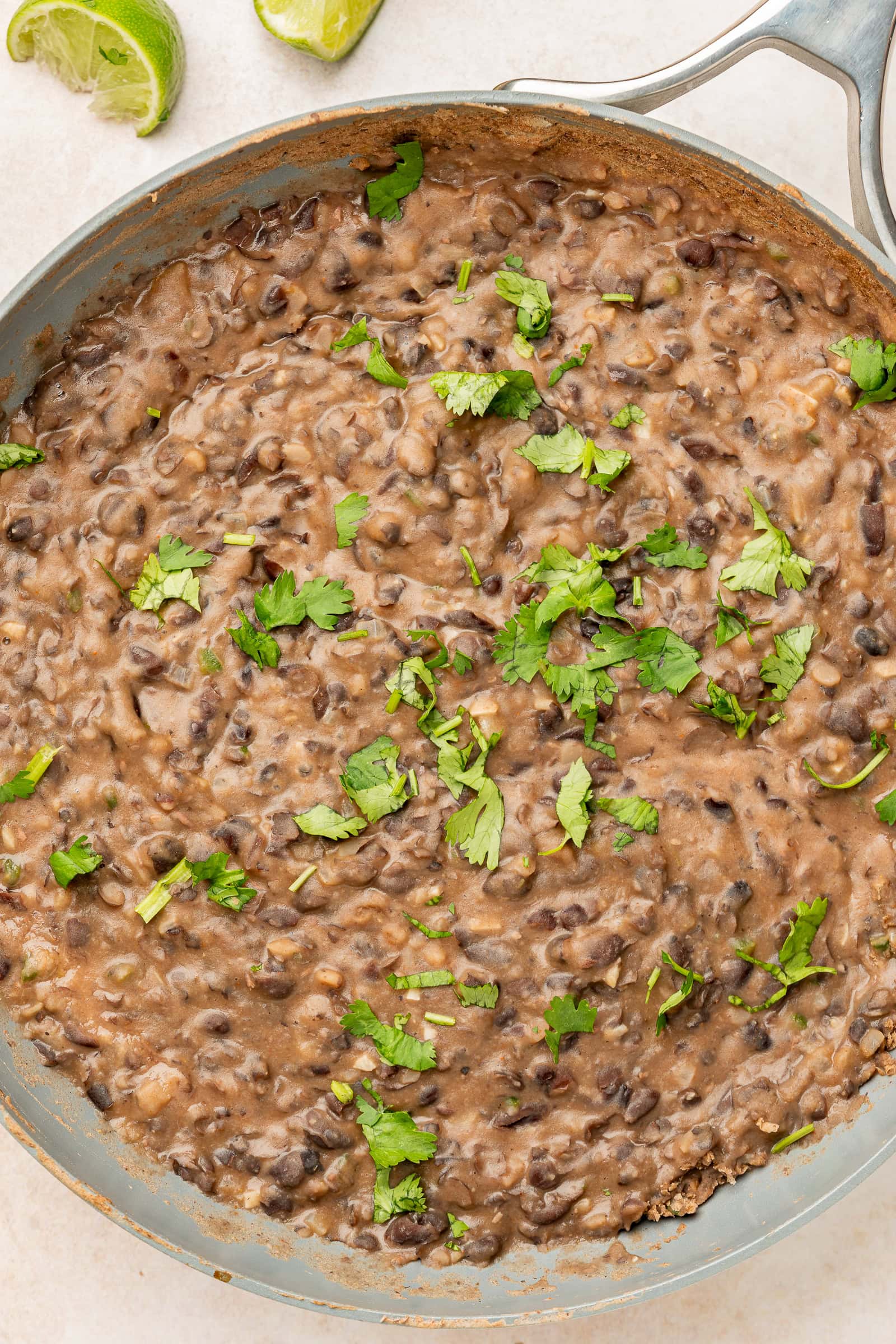 Cilantro garnished refried black beans in a frying pan.