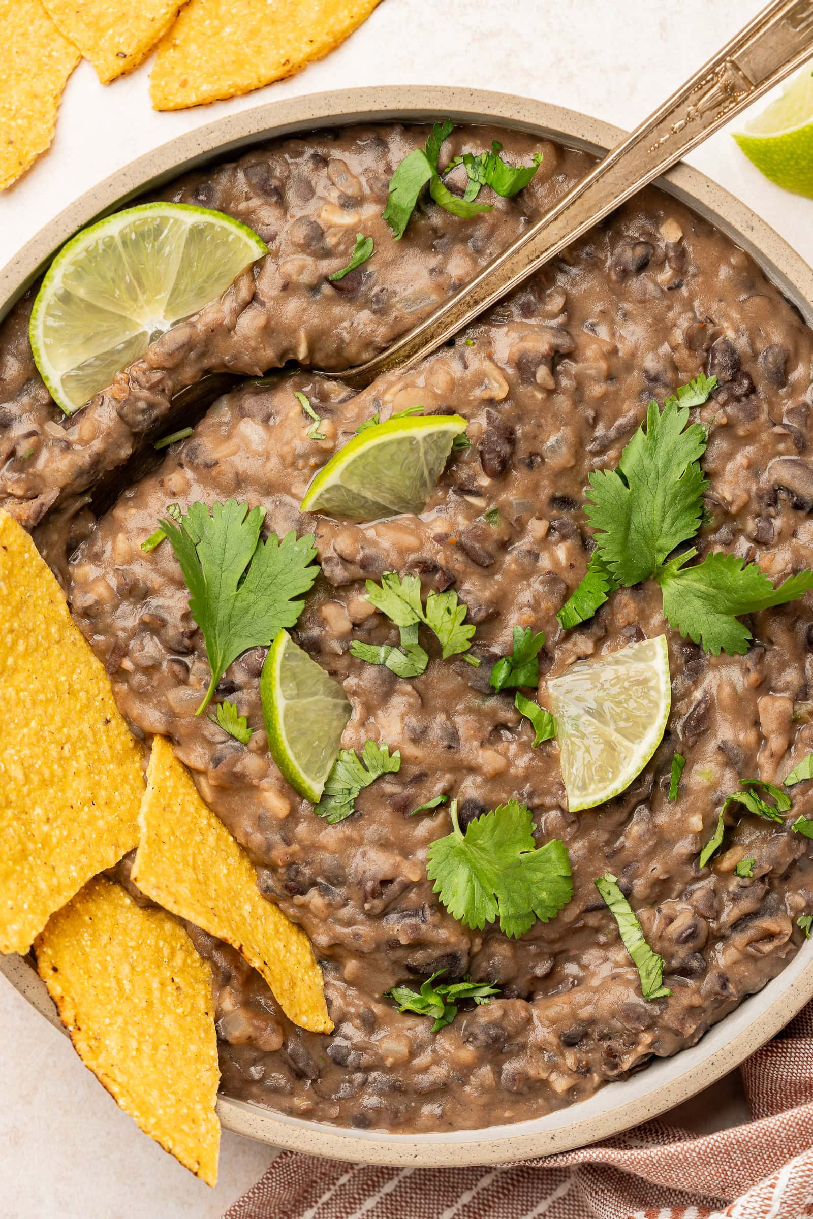 Refried black beans in serving dish garnished with lime and cilantro and served with tortilla chips.